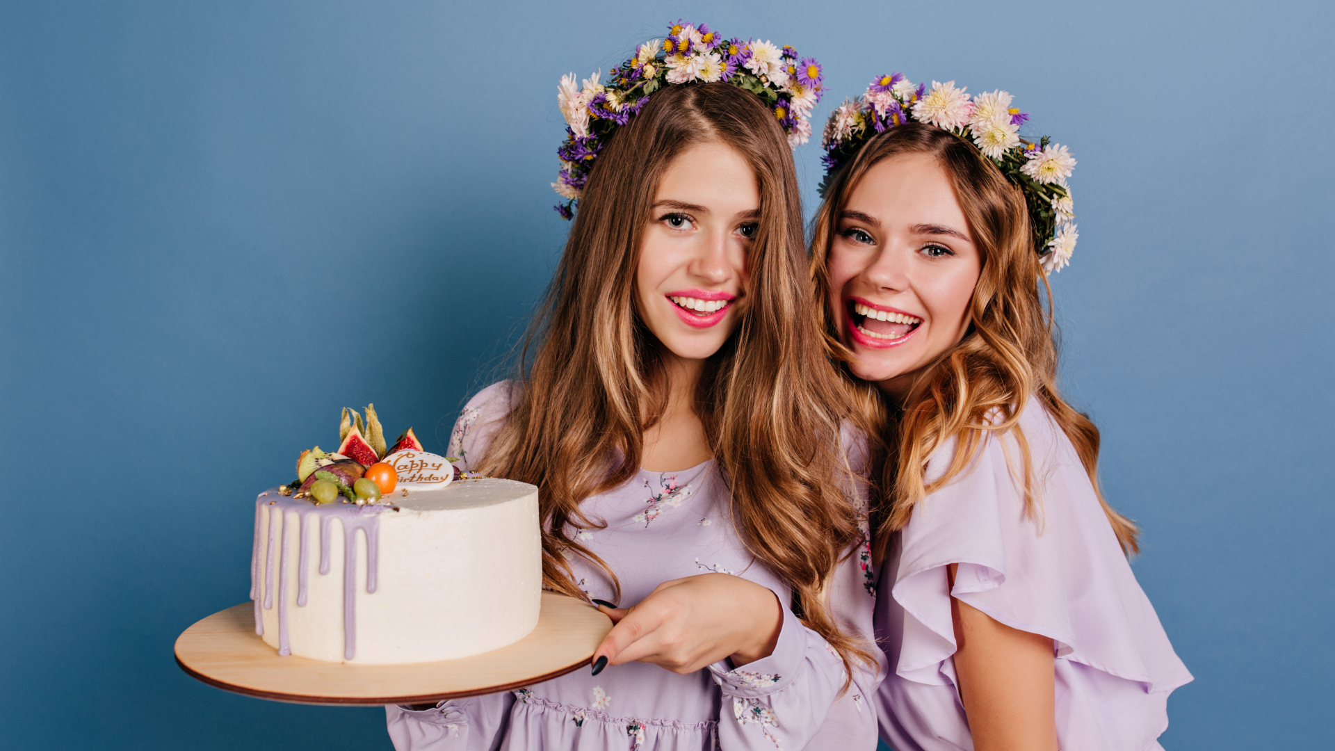 Две веселые молодые девушки с тортом на голубом фоне