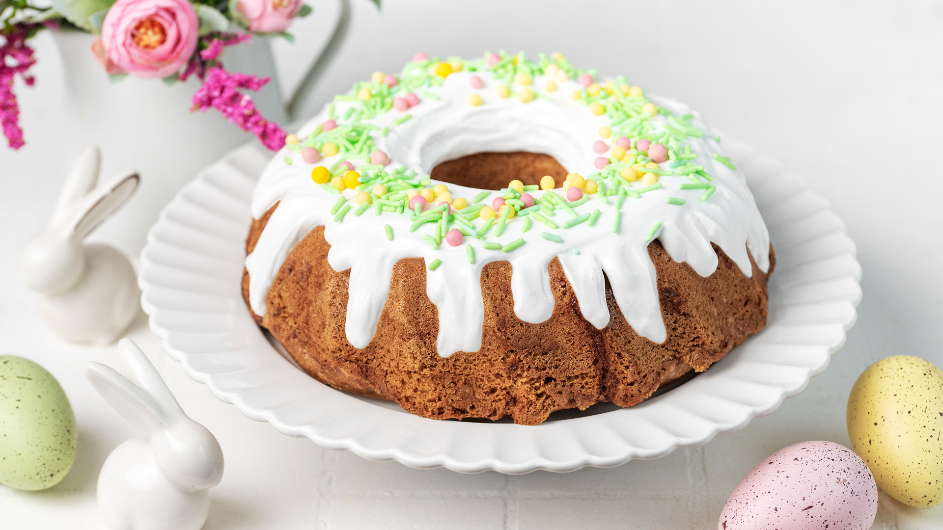 Сладкий пасхальный кулич с яйцами и цветами на столе