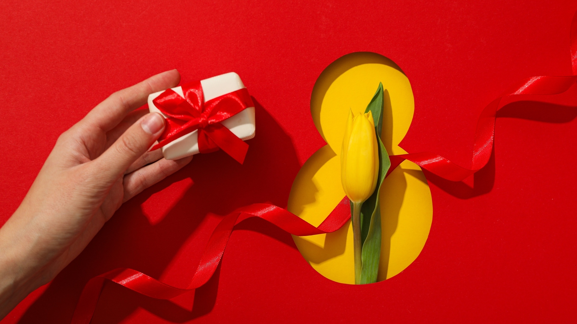 Красный фон с подарком, желтым тюльпаном и цифрой на 8 марта