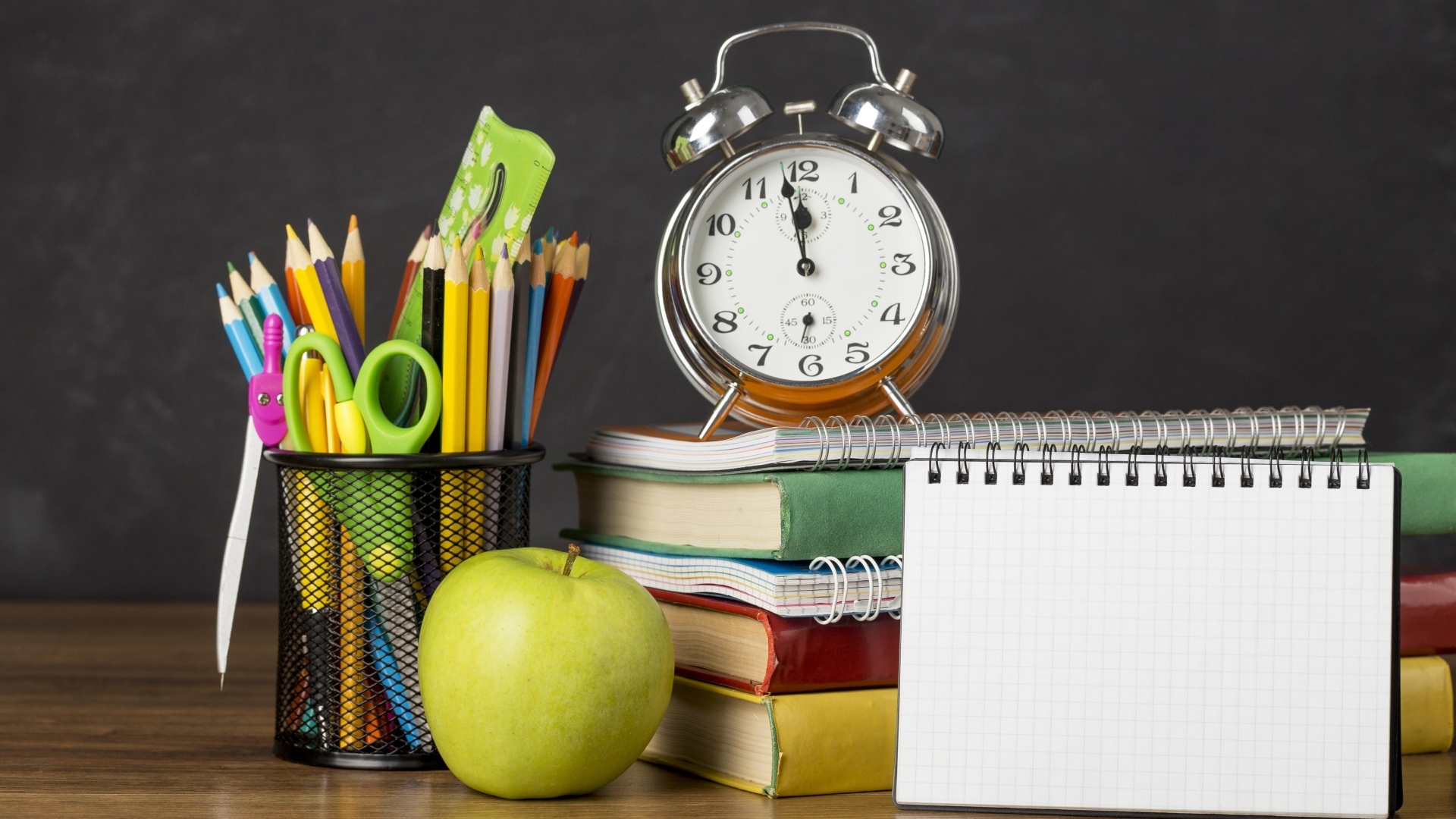 Канцелярские предметы на столе с будильником и книгами 