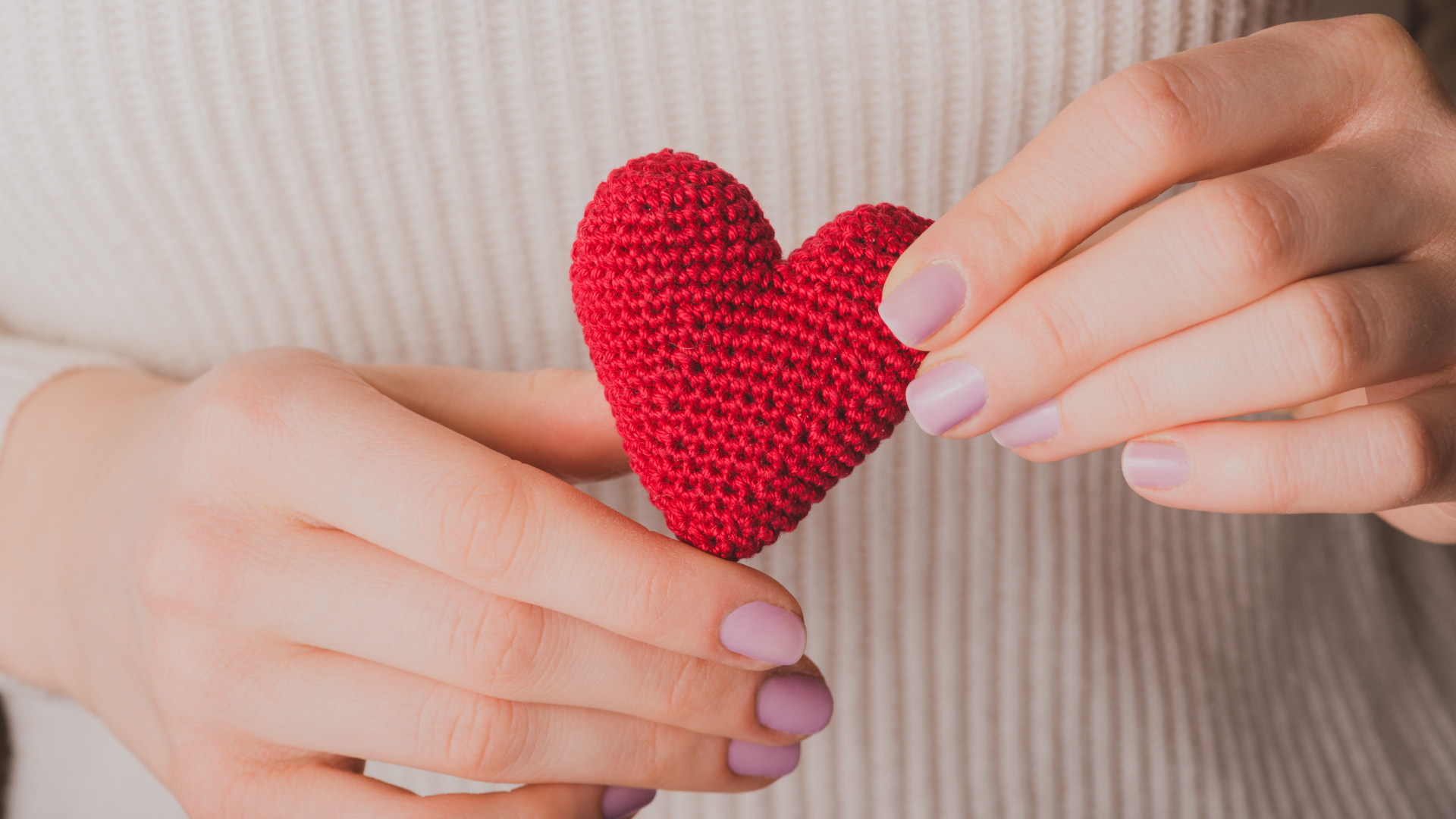 Девушка держит в руке вязаное красное сердце