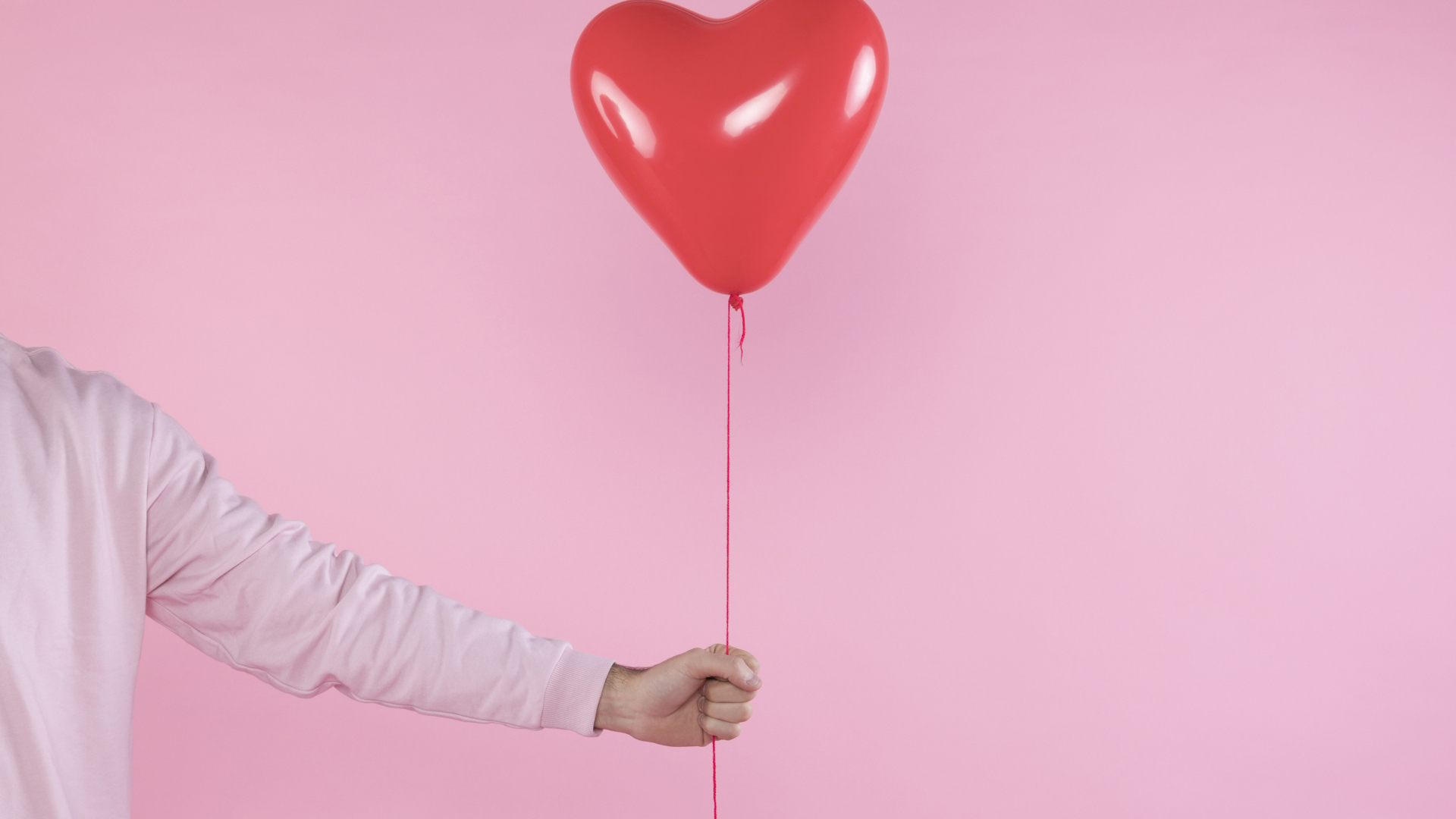 Шарик в форме сердца в руке на розовом фоне