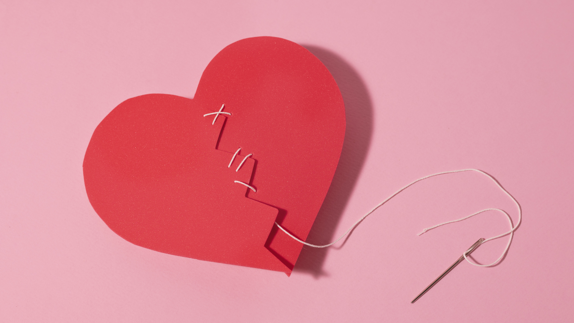 Бумажное сердце сшили нитками на розовом фоне
