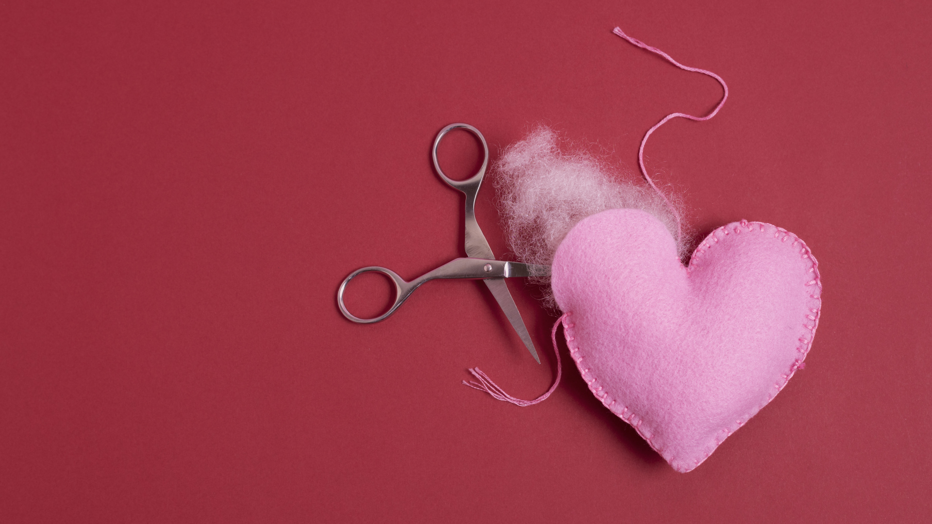 Розовое  сердце с ножницами на красном фоне