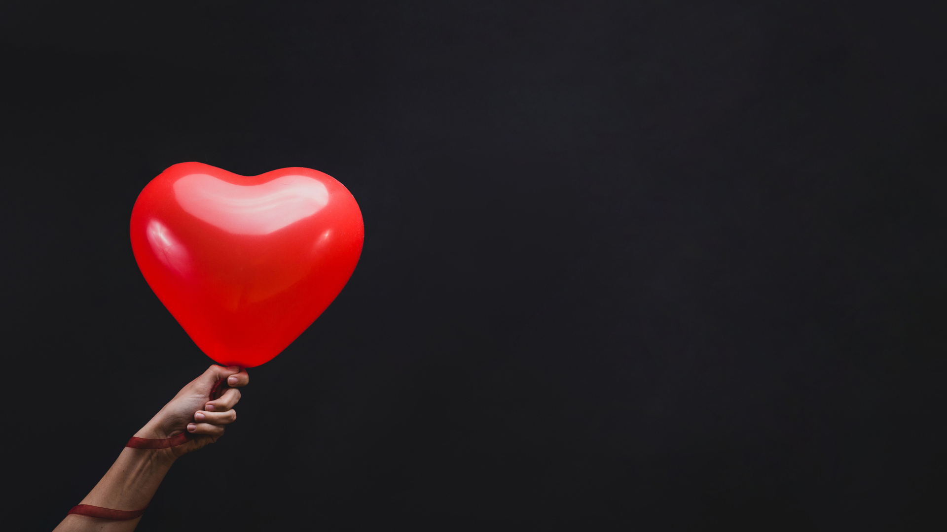 Красный шарик в форме сердца на черном фоне
