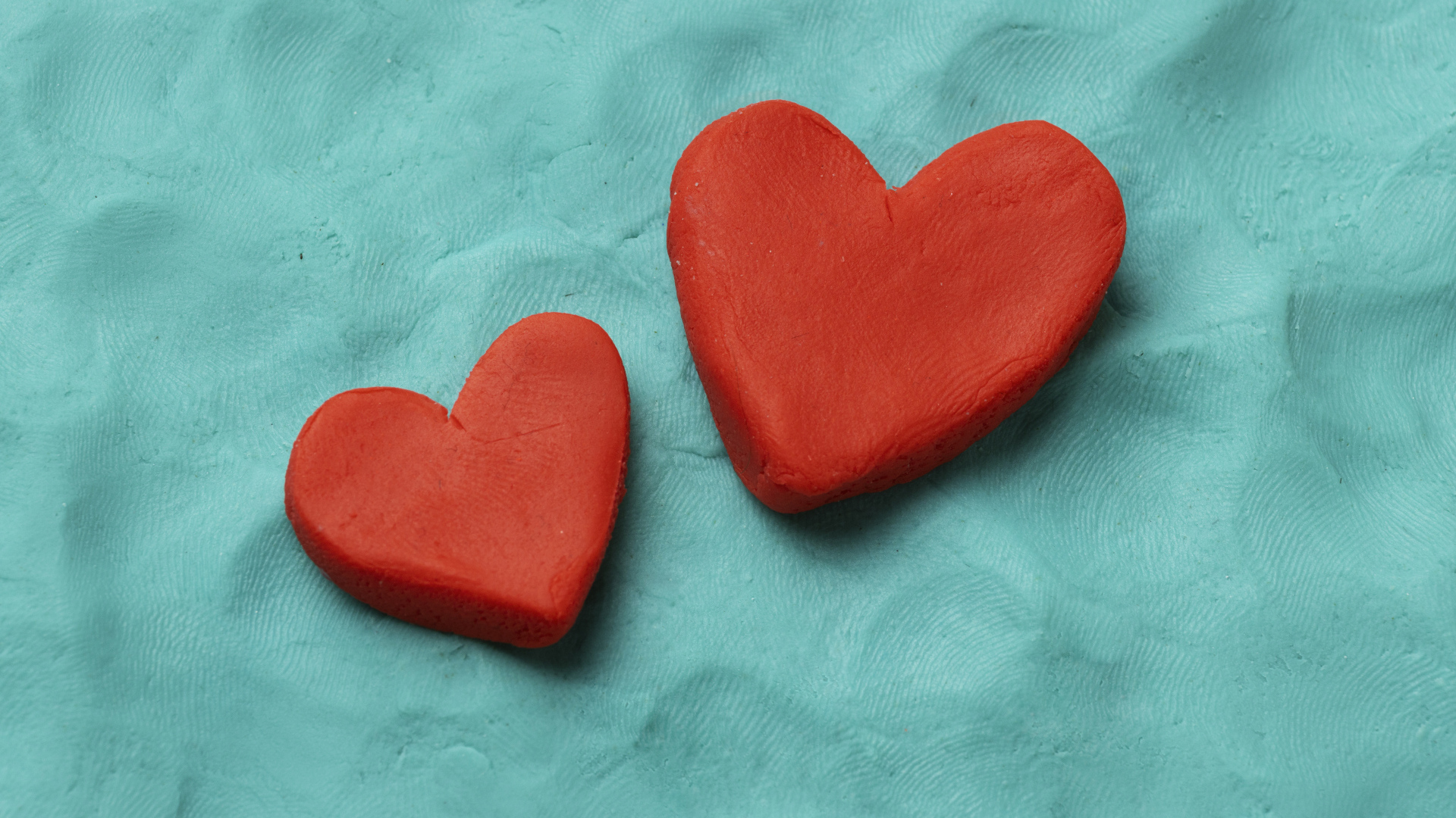 Два красных сердца из пластилина на голубом фоне
