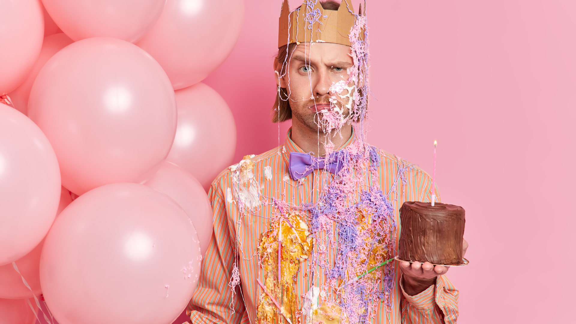 Мужчина принц с тортом и шариками на розовом фоне