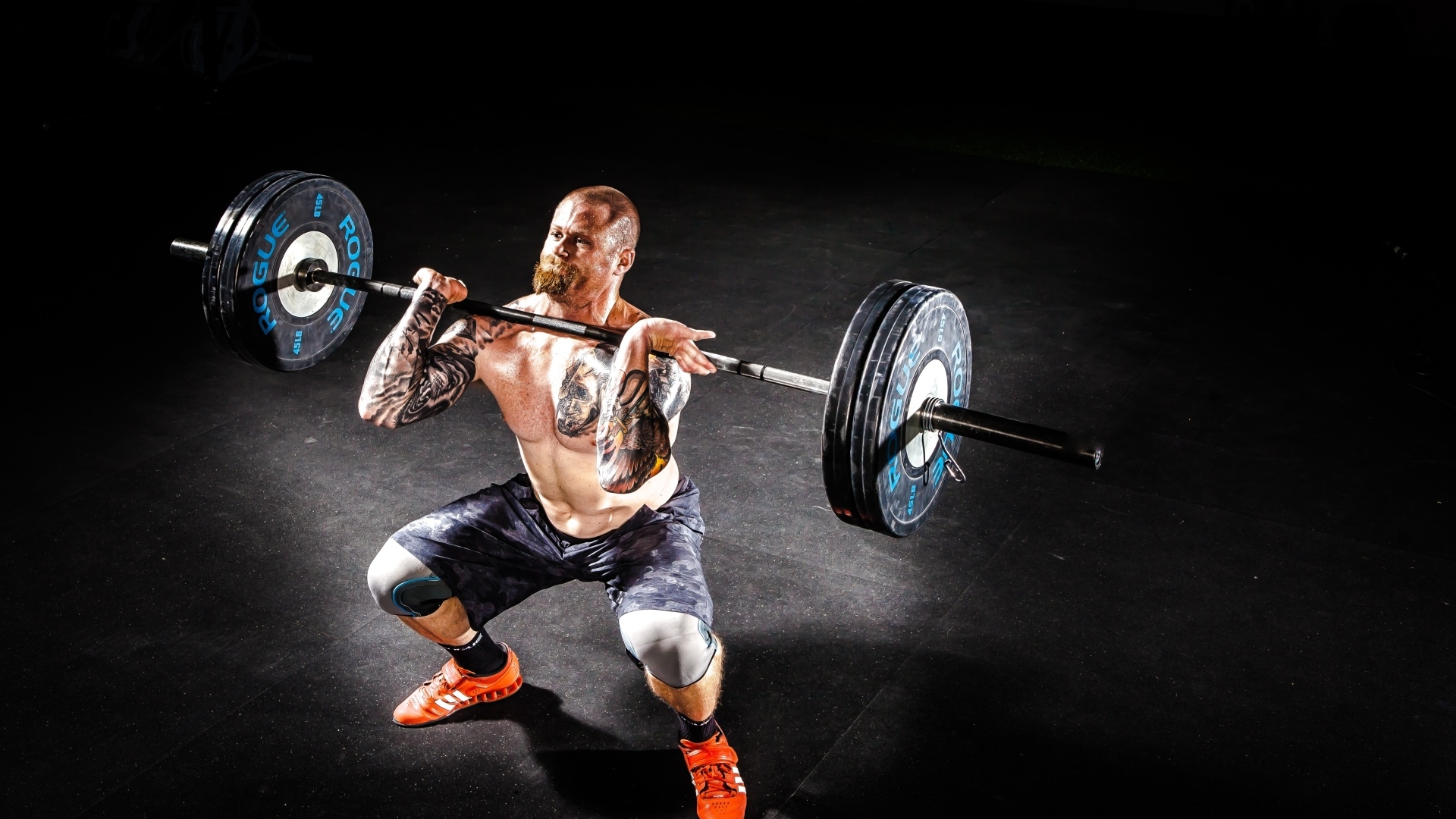 Сильный мужчина с татуировками на теле поднимает штангу