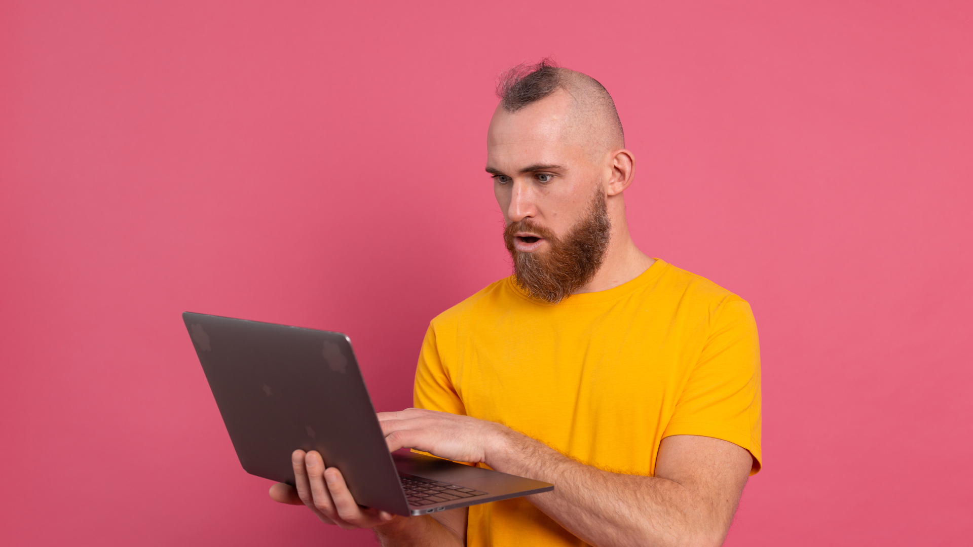 Удивленный мужчина с ноутбуком на розовом фоне