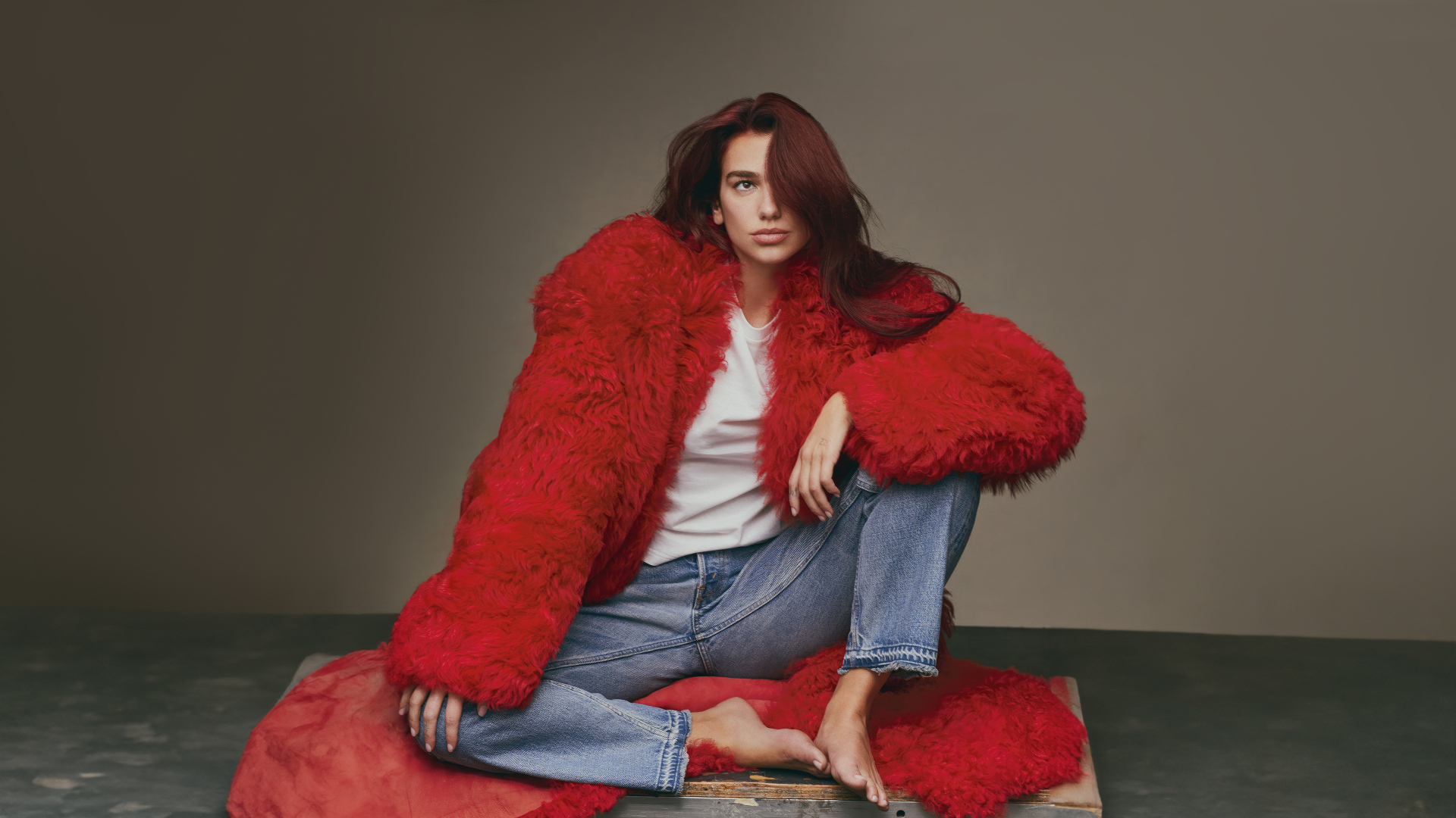 Певица Дуа Липа в красной шубе сидит на полу