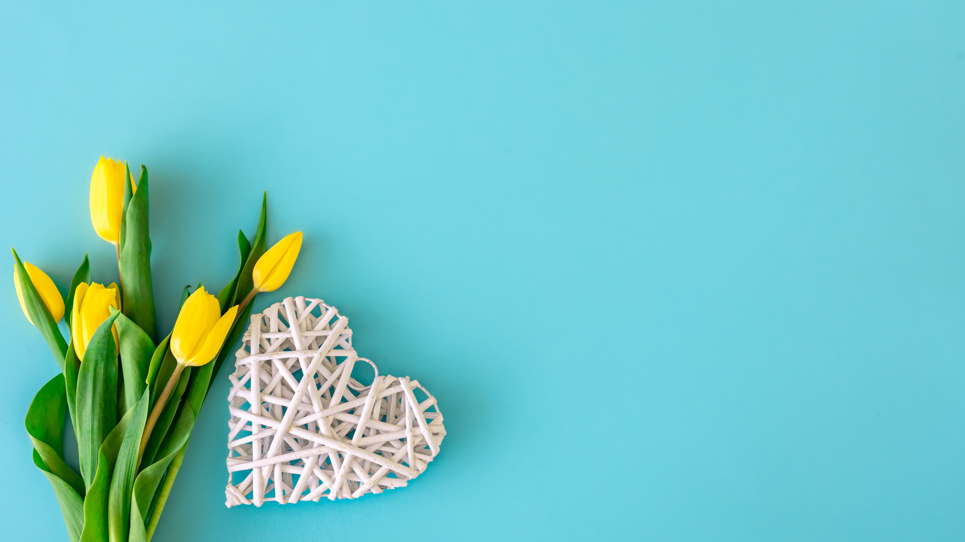 Белое плетеное сердце с букетом желтых тюльпанов на голубом фоне