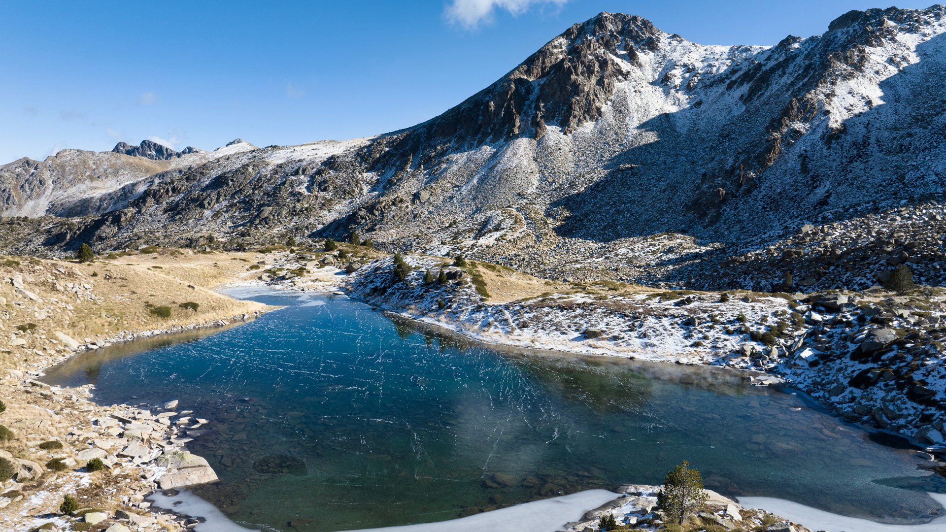 Покрытое льдом озеро в заснеженных горах в лучах солнца, Андорра