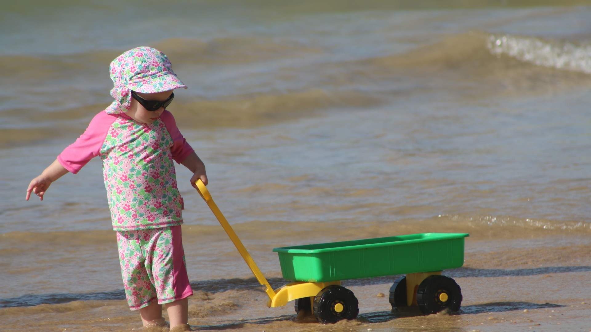 Девочка с машинкой играет на песке у моря