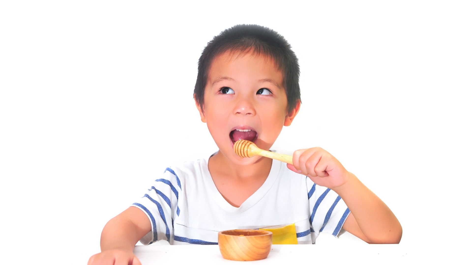 Мальчик азиат ест мед на сером фоне