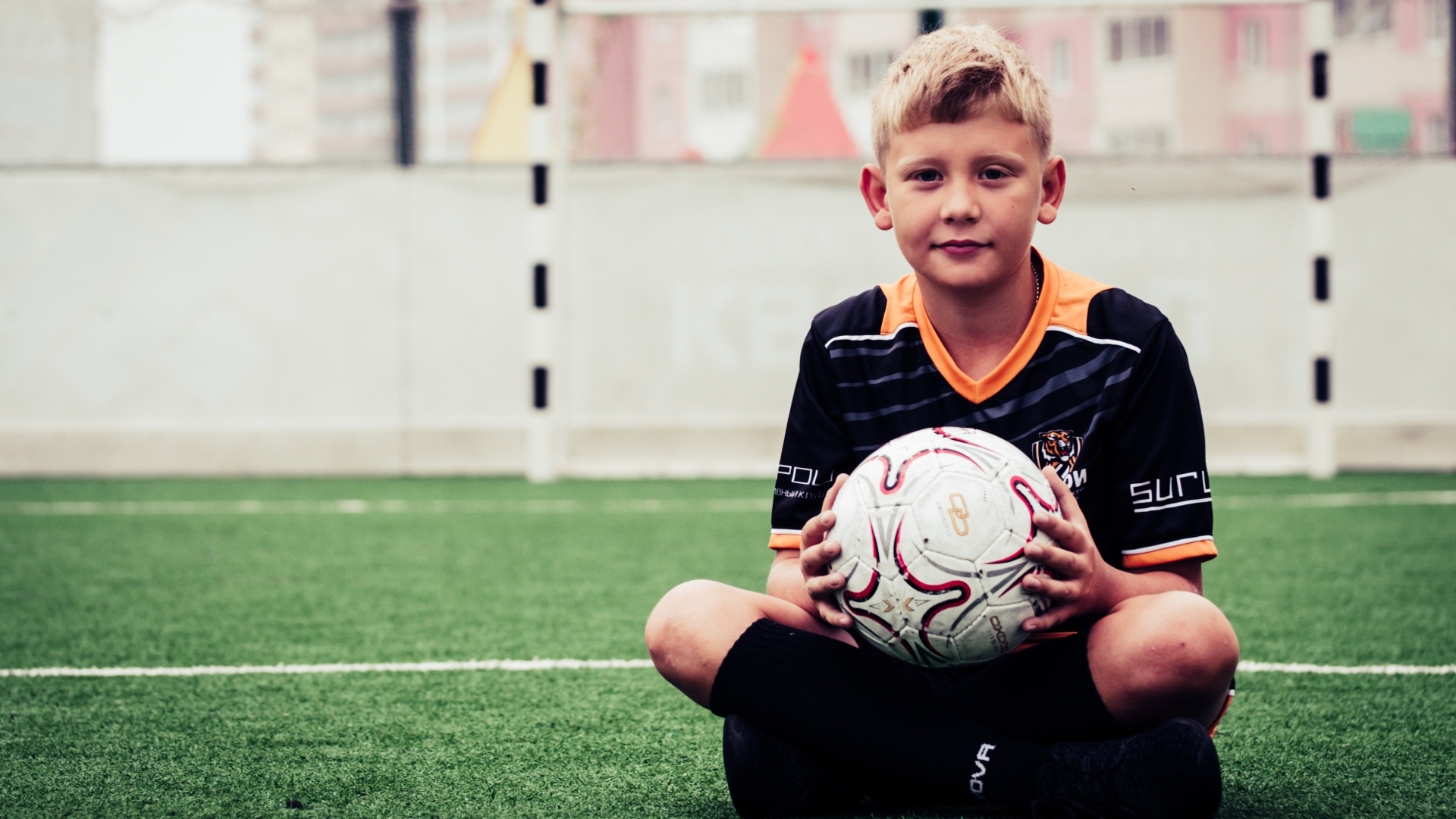 Мальчик футболист сидит на траве с мячом