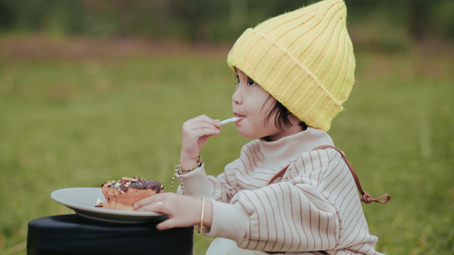 Маленькая девочка в желтой шапке ест пирожное