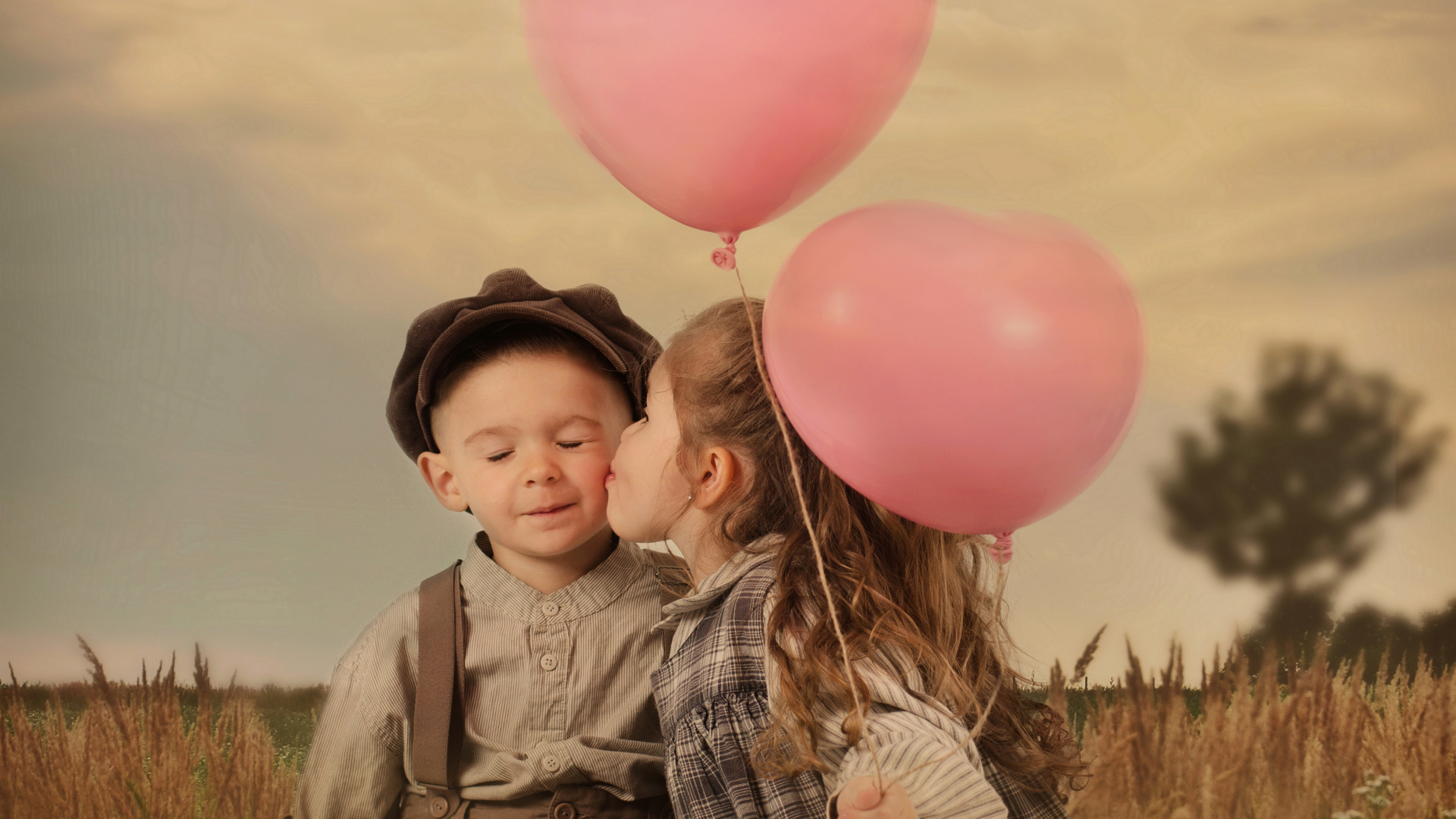 Маленькая девочка с шариками целует мальчика