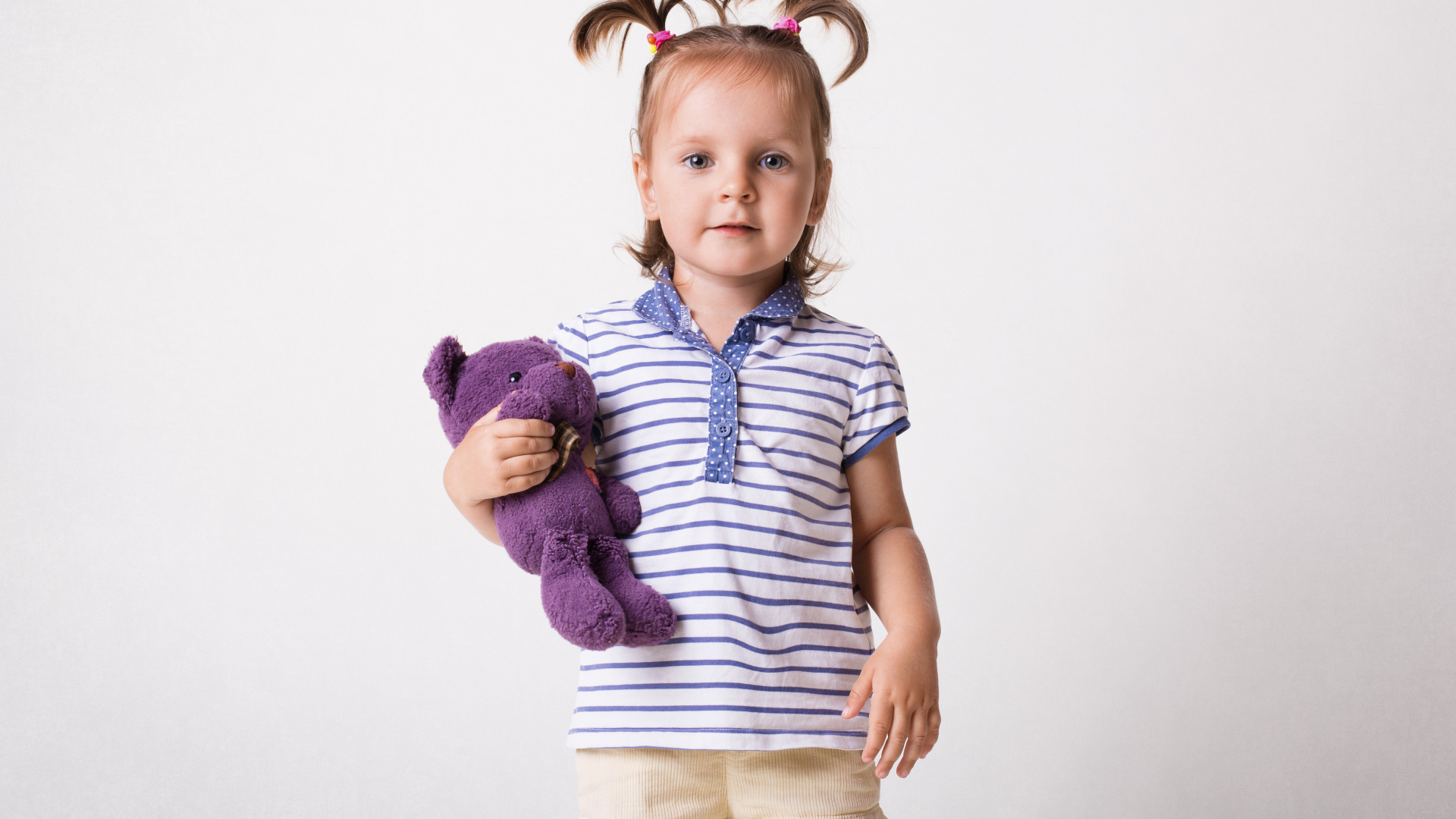 Маленькая девочка с игрушечным медведем на сером фоне