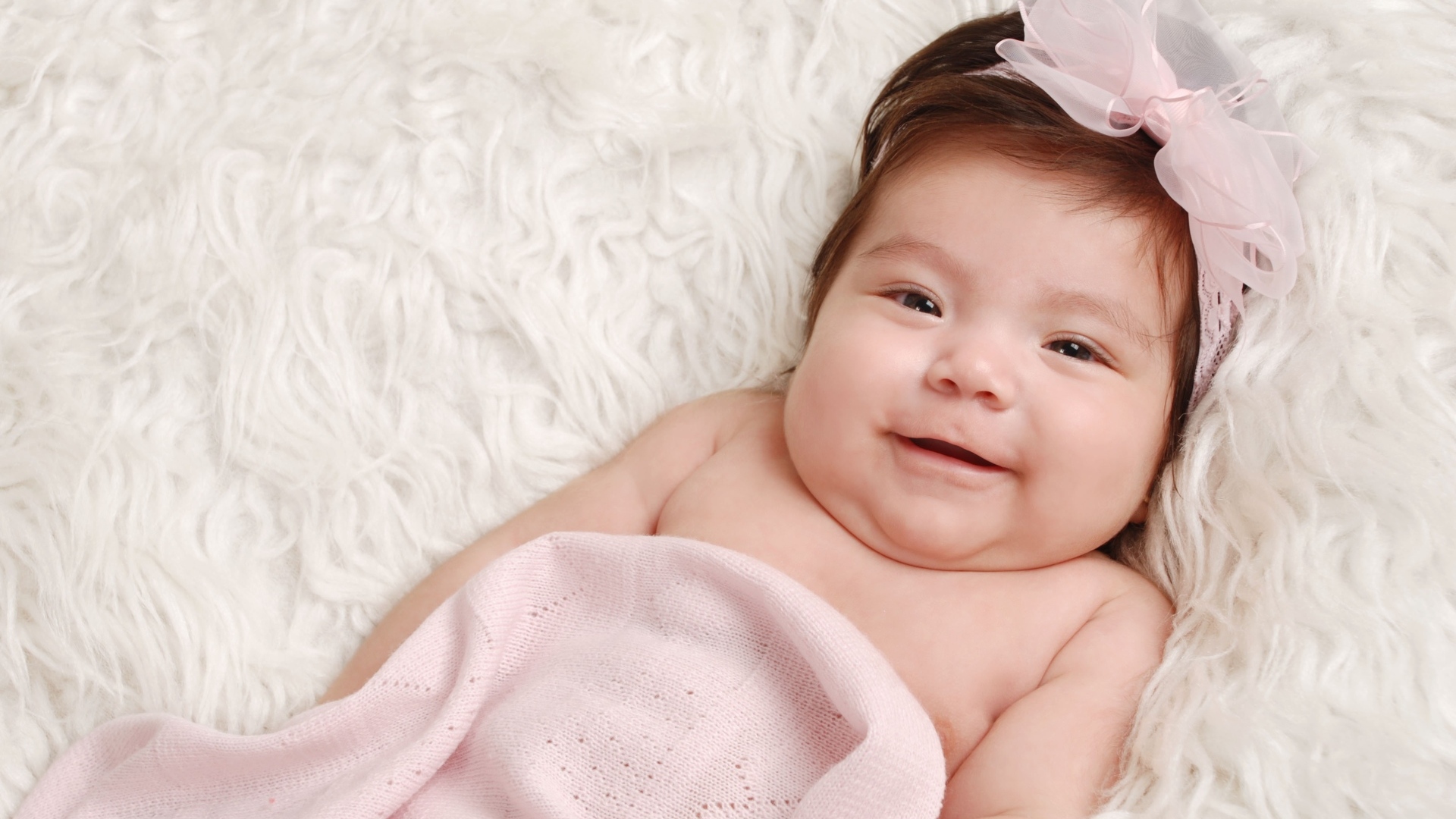 Улыбающаяся новорожденная малышка с бантом на голове