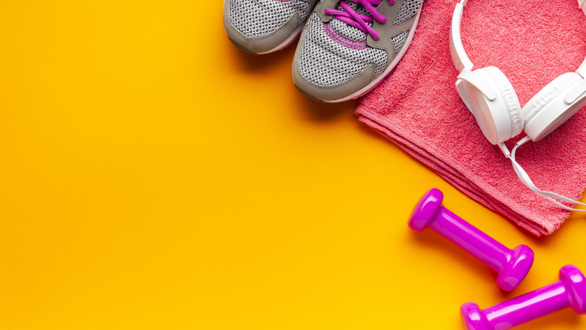Розовые гантели, наушники, кроссовки и полотенце на желтом фоне