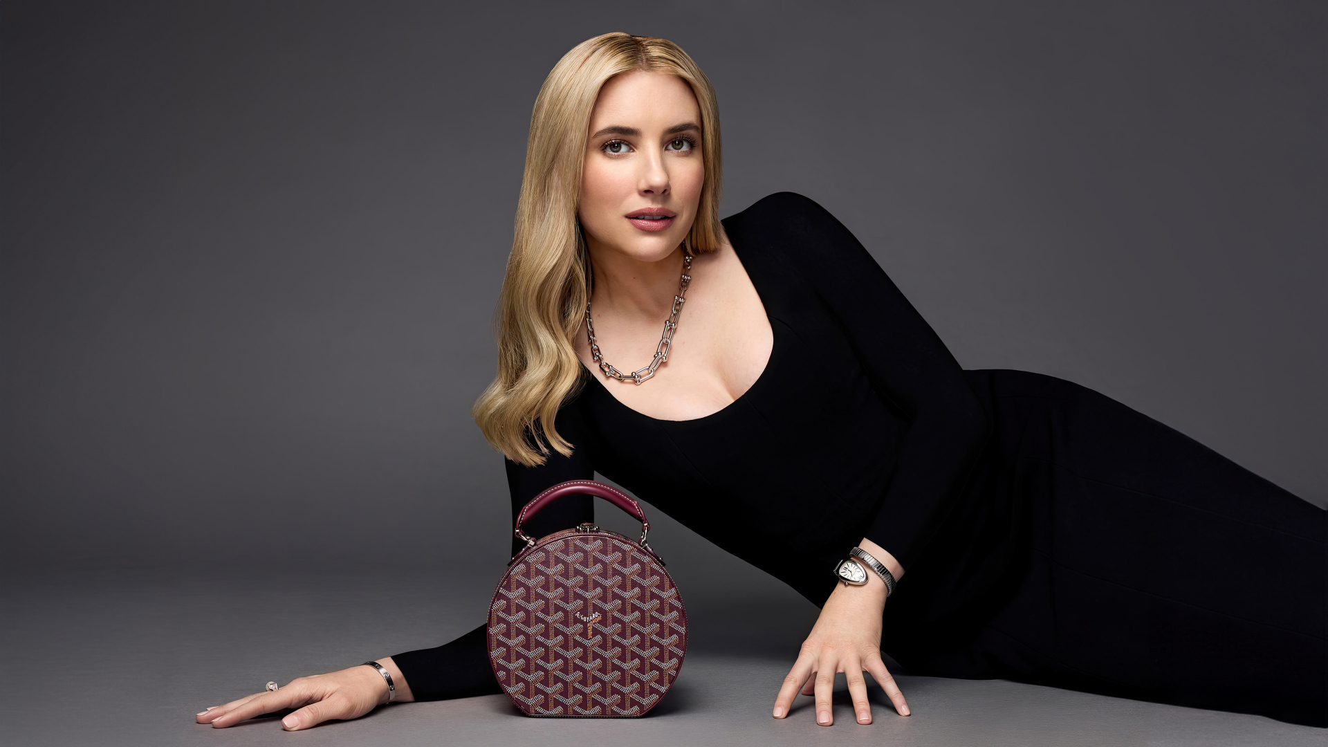 Актриса Эмма Робертс в черном платье с сумочкой лежит на сером фоне