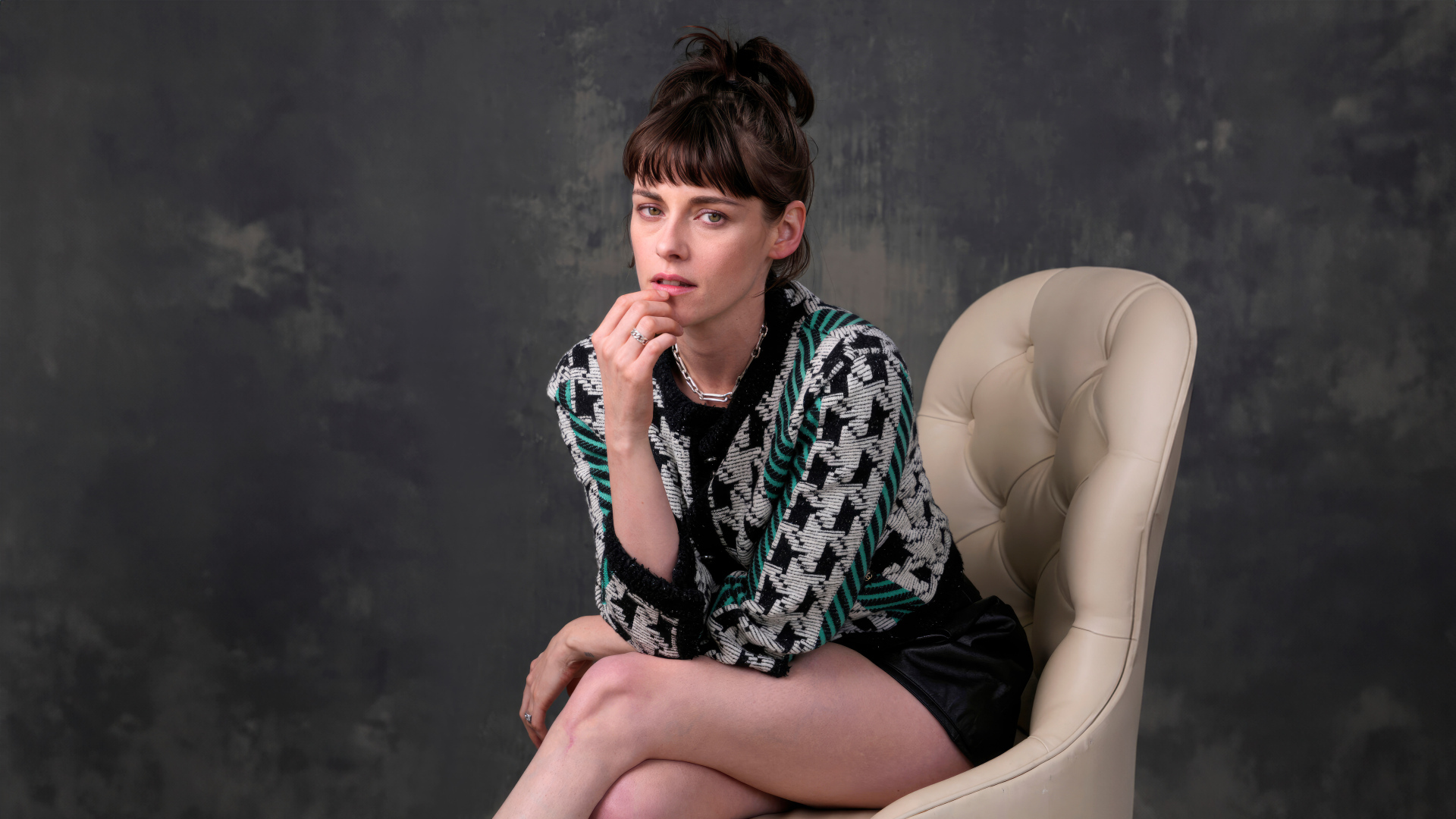 Актриса Кристен Стюарт сидит в кресле на фоне серой стены