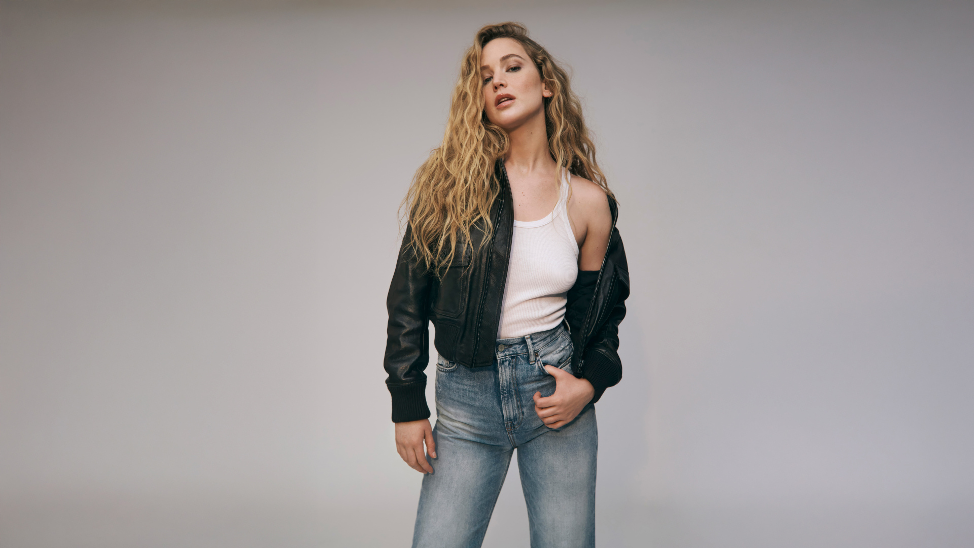 Американская актриса Дженнифер Лоуренс  в джинсах на сером фоне