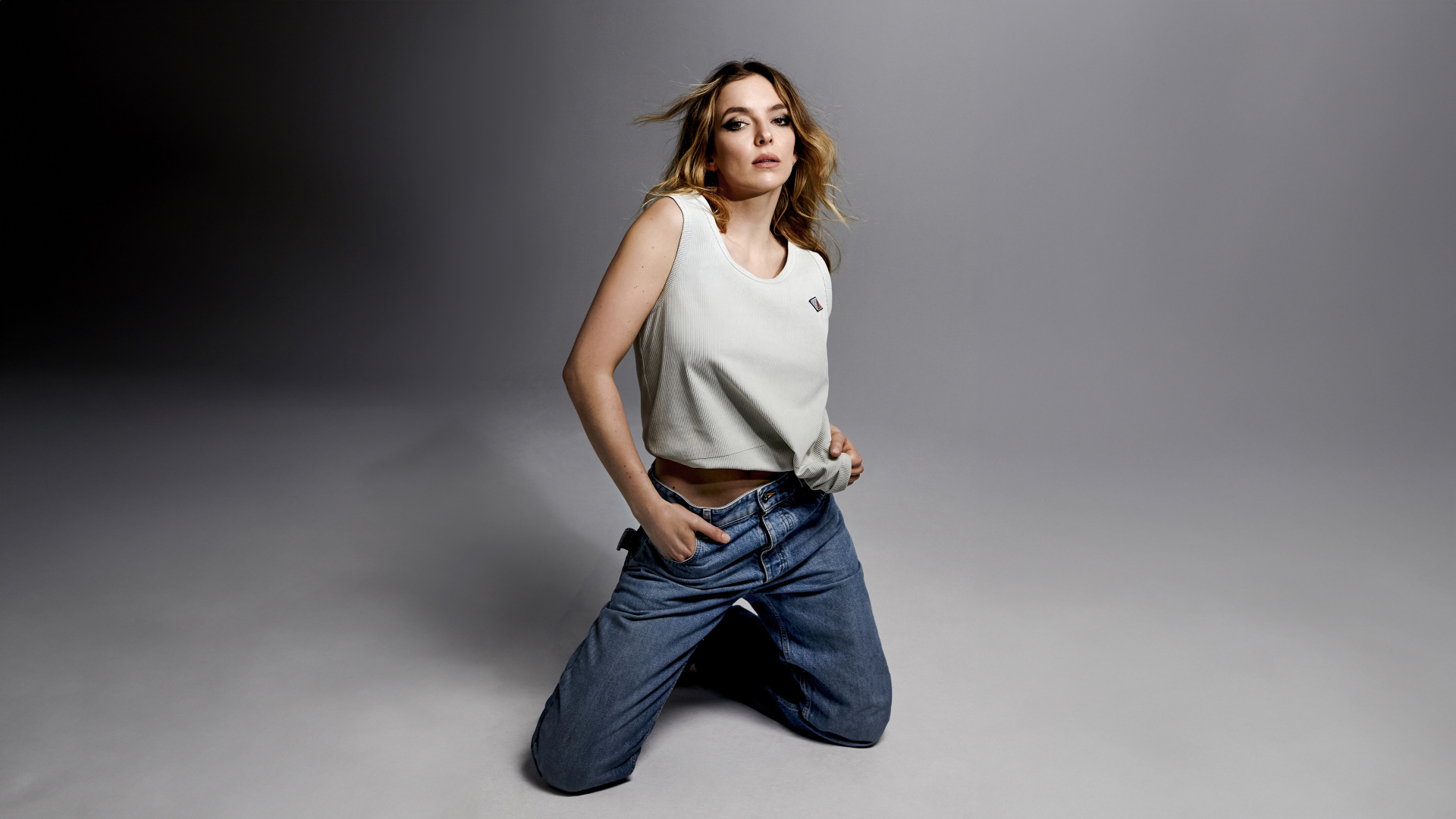 Британская актриса Джоди Комер в джинсах на сером фоне
