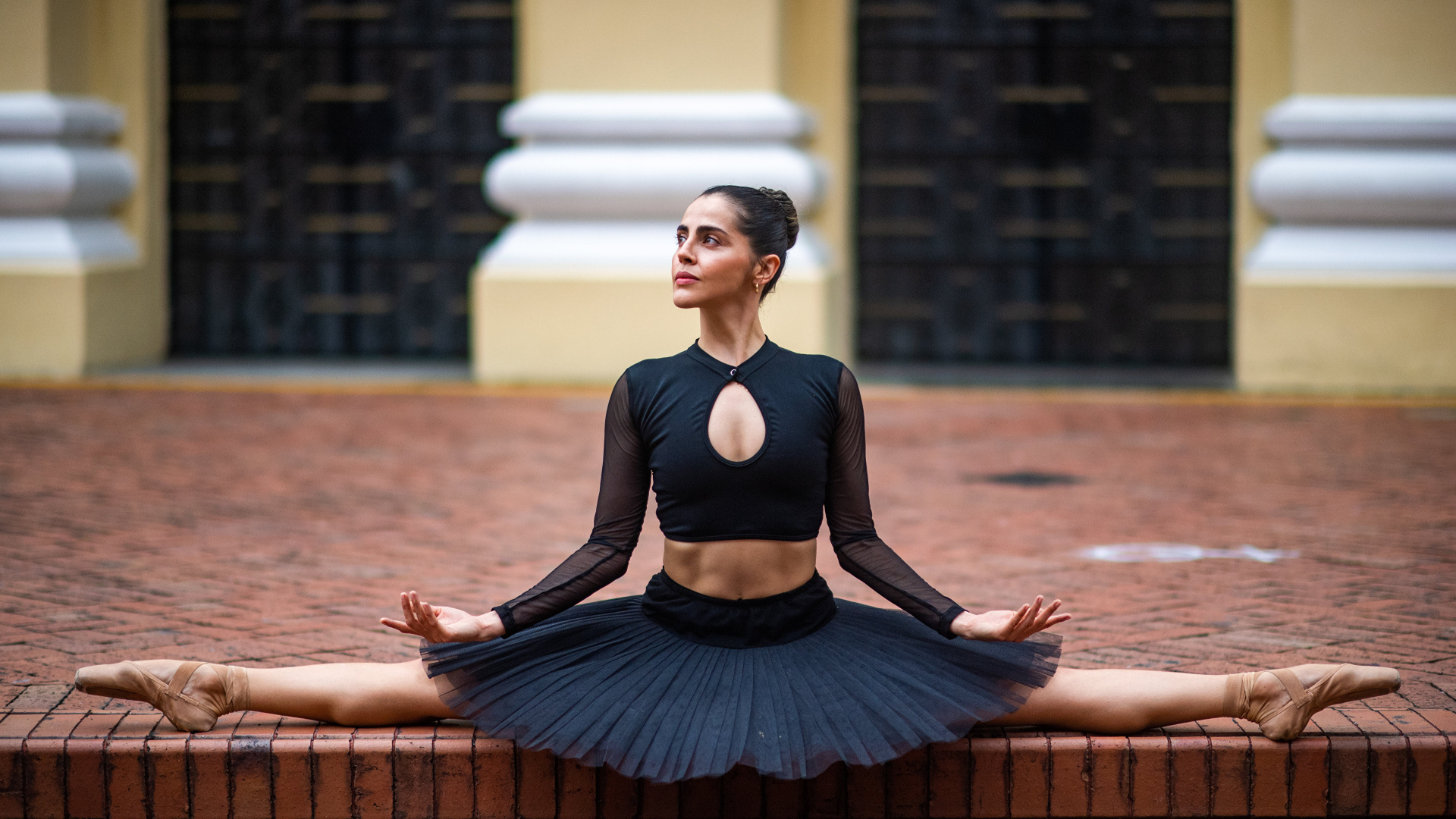 Девушка балерина в черном сидит на шпагате