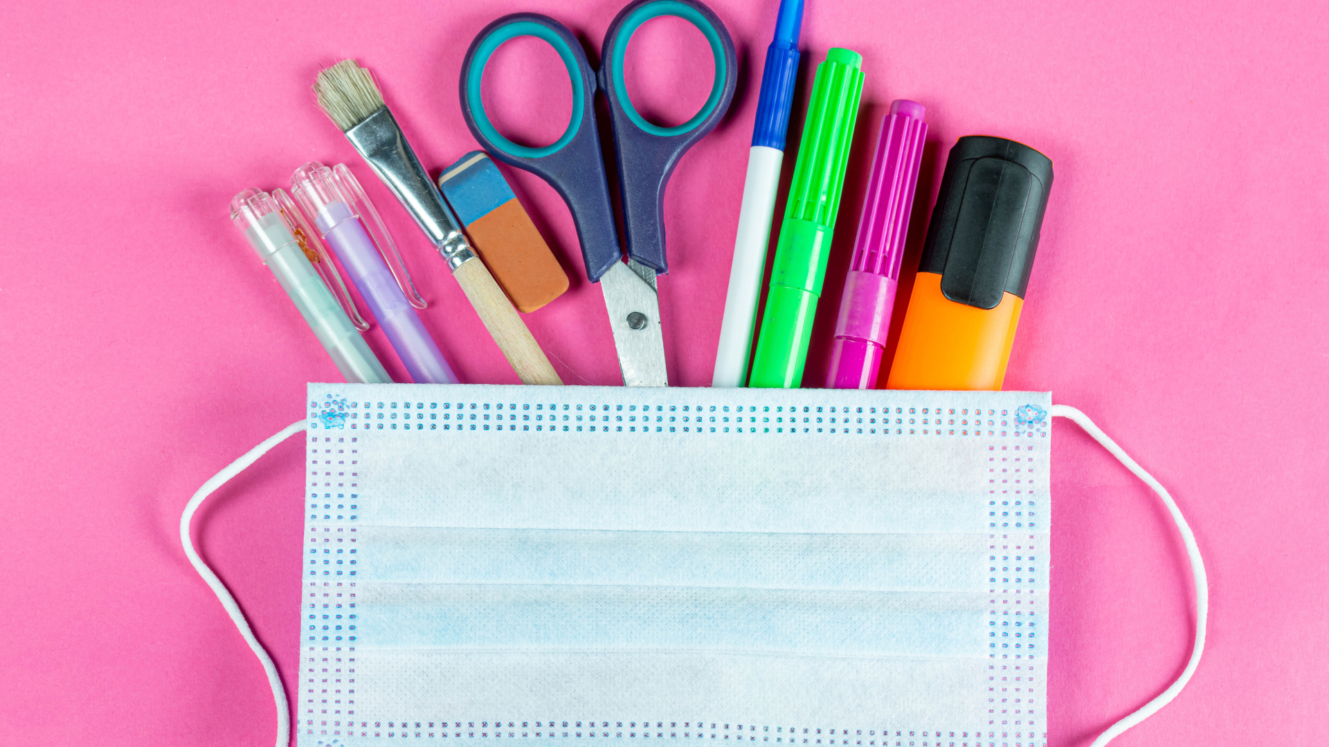 Канцелярские предметы и медицинская маска на розовом фоне