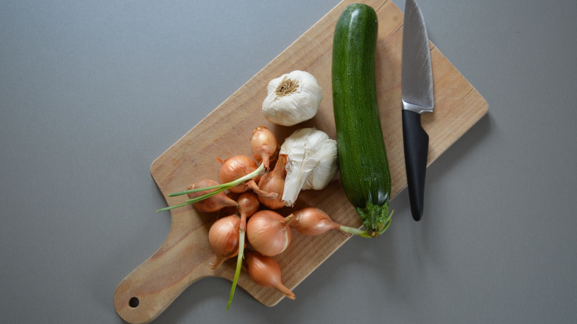 Лук, чеснок и кабачок на разделочной доске с ножом