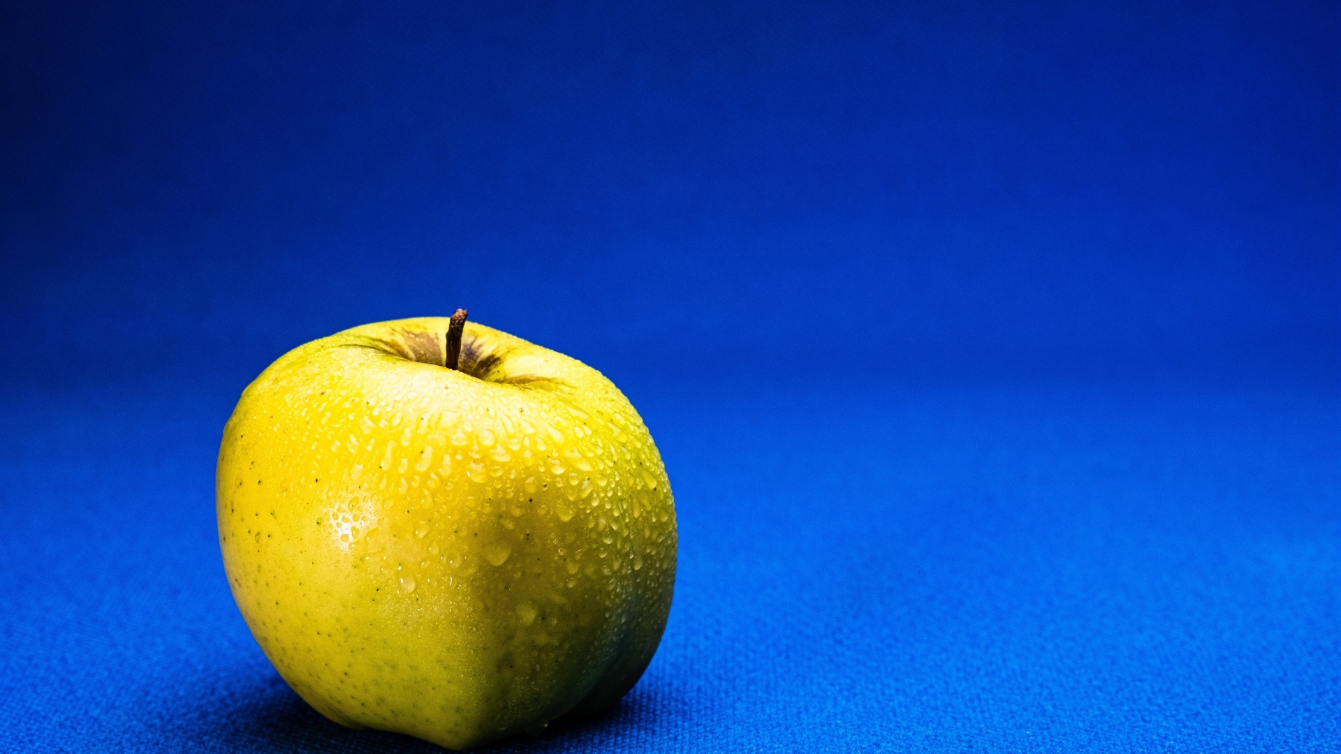 Большое желтое мокрое яблоко на синем фоне
