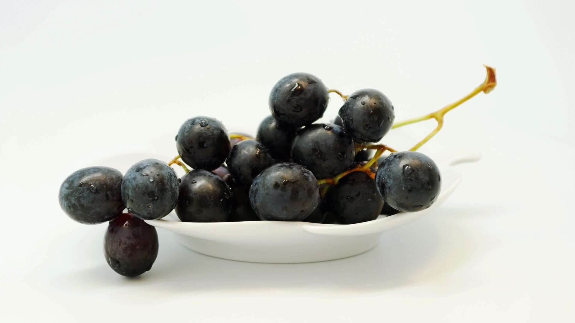 Гроздь синего винограда в тарелке на белом фоне