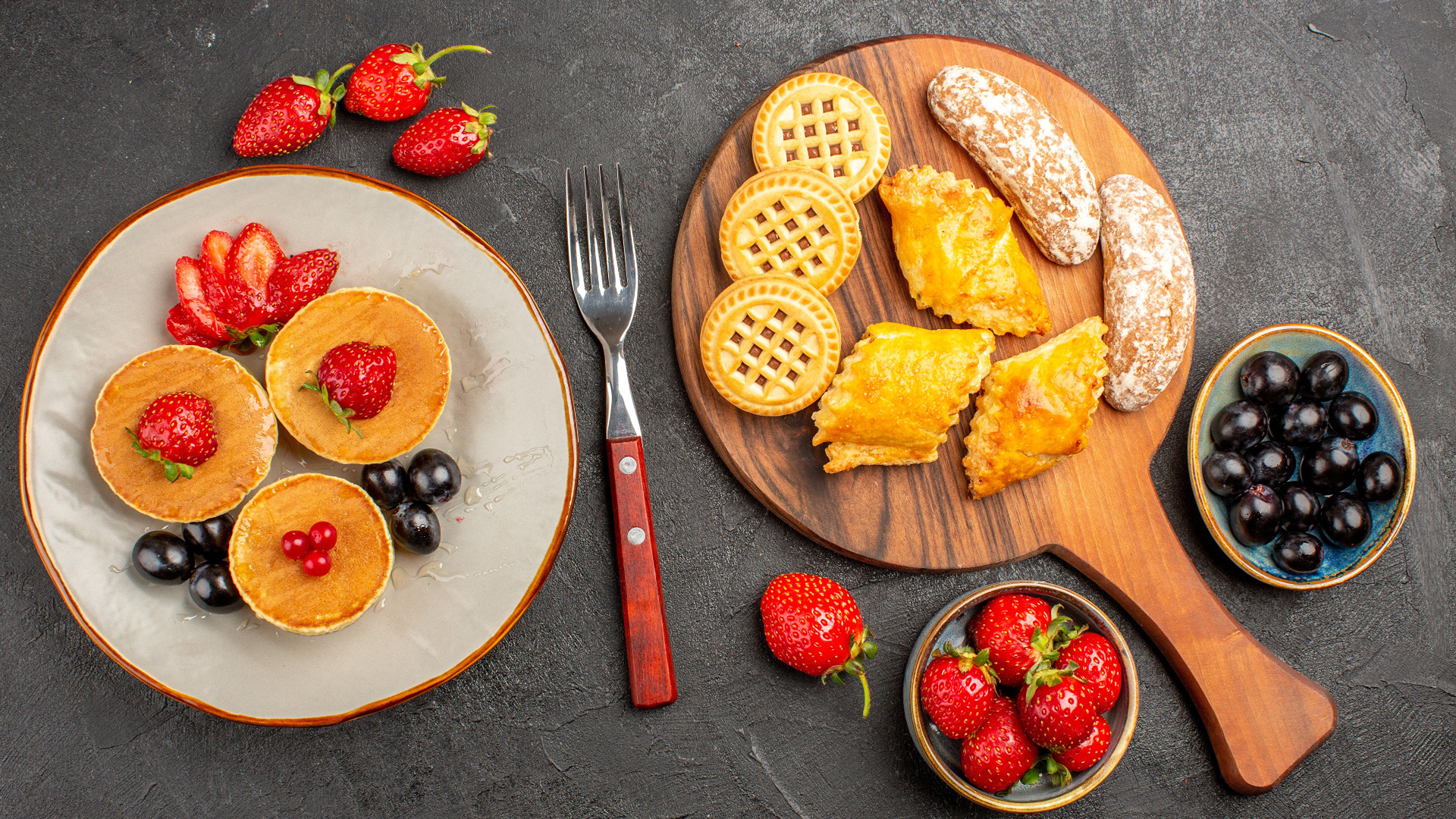 Печенье и оладьи на столе с ягодами клубники и виноградом