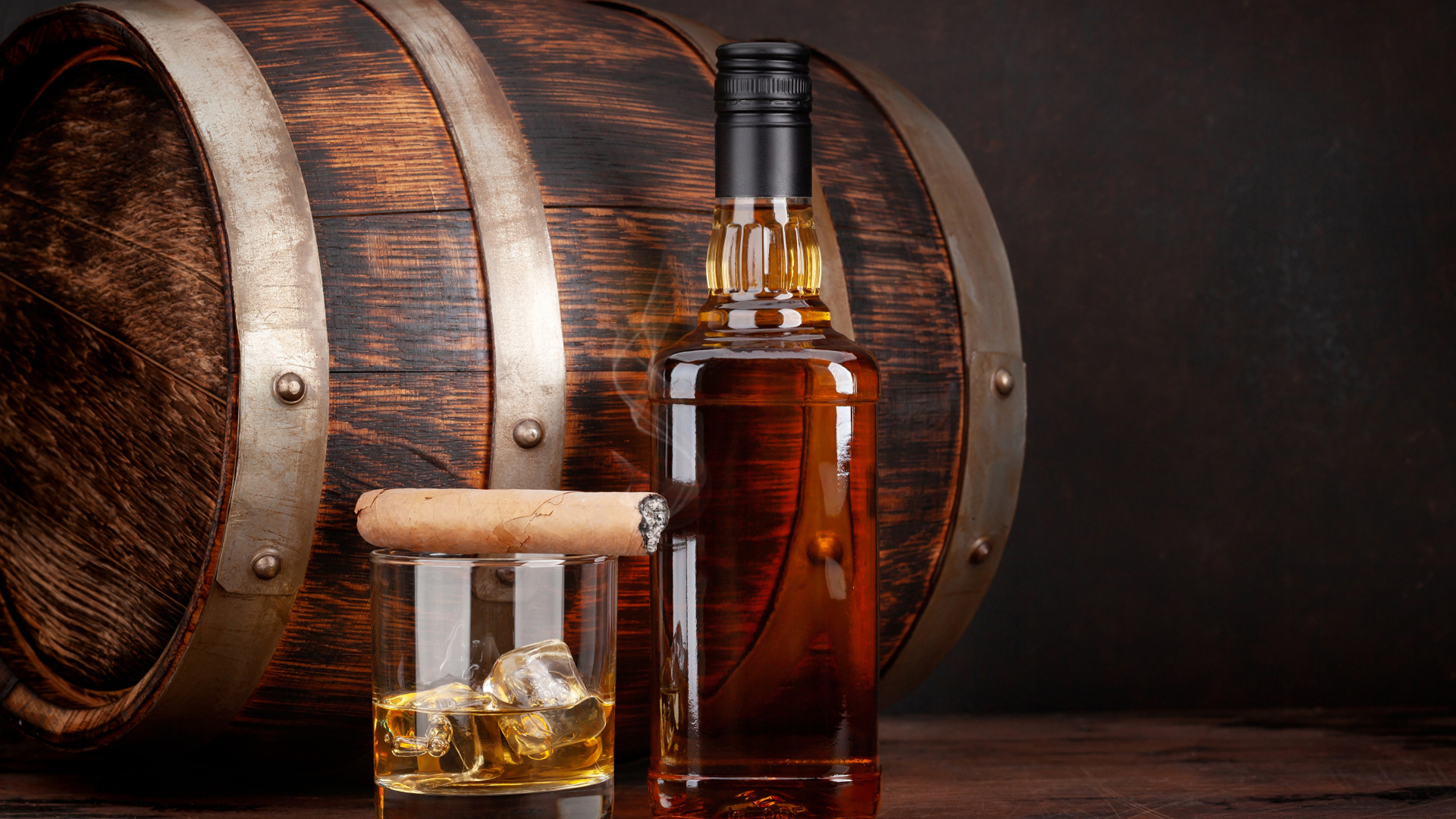 Бутылка виски на столе со стаканом, сигарой и бочкой