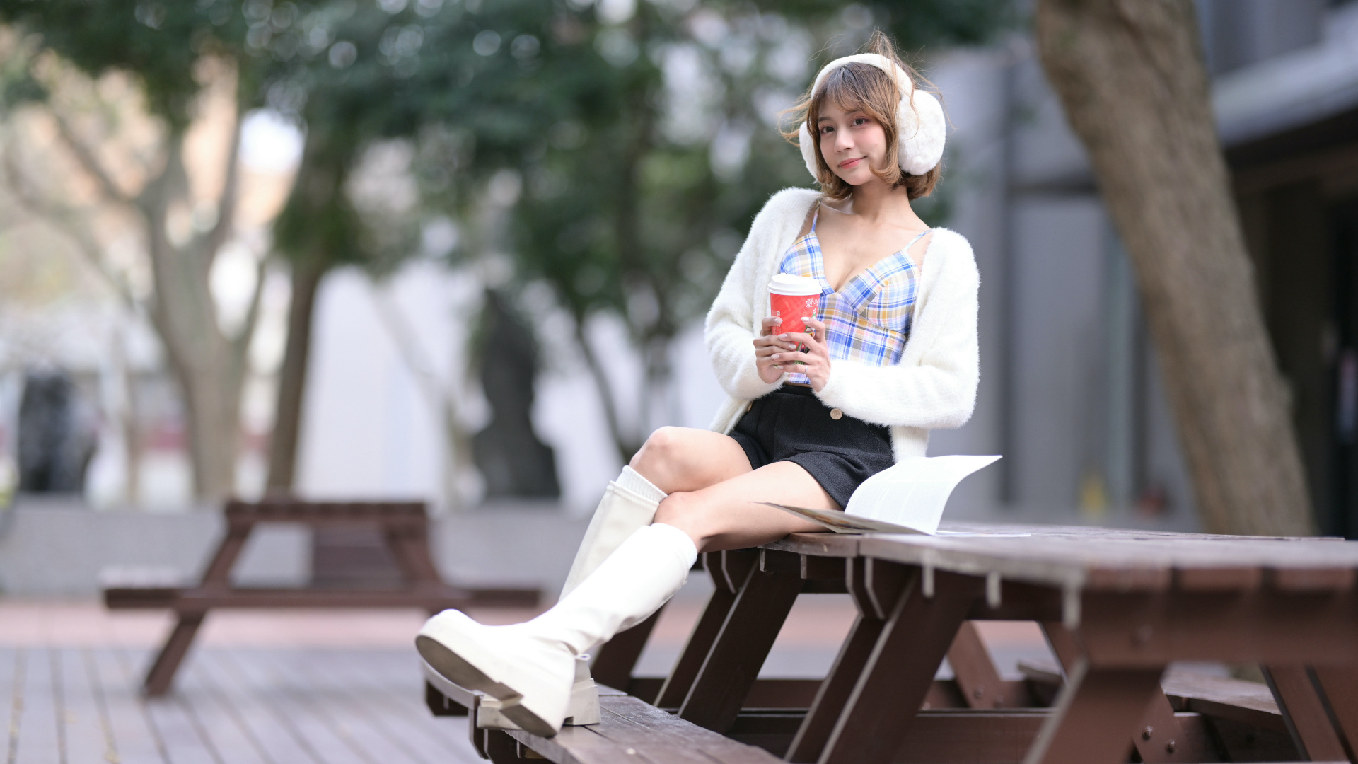 Девушка азиатка с кофе сидит на столе в парке