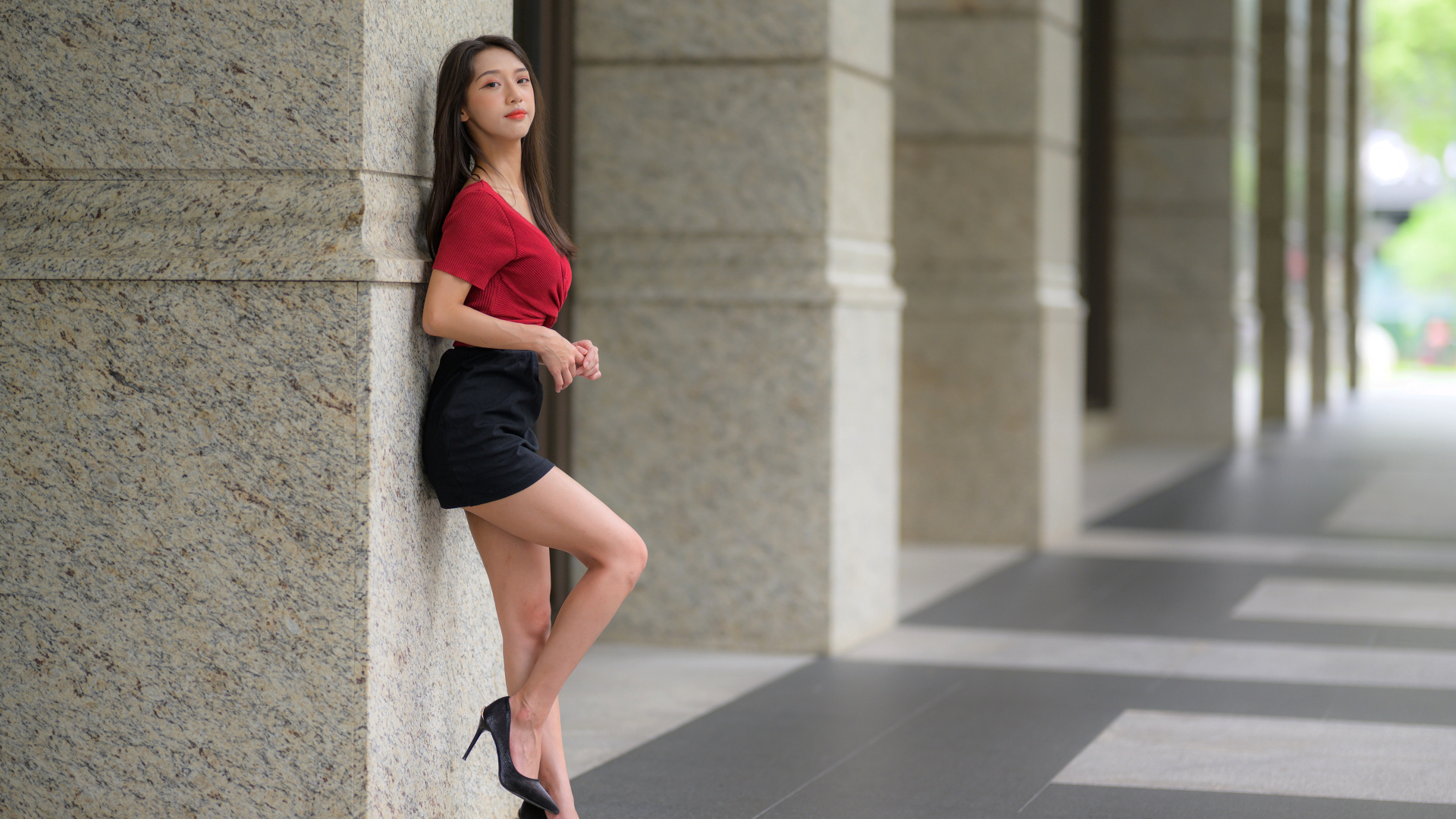 Азиатка в короткой черной юбке стоит у стены