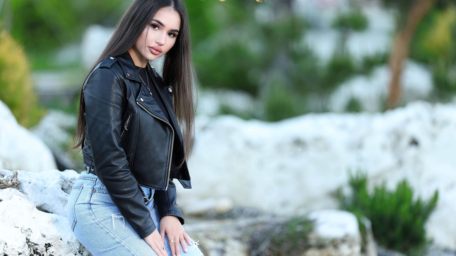 Брюнетка в черной кожаной куртке сидит на камне