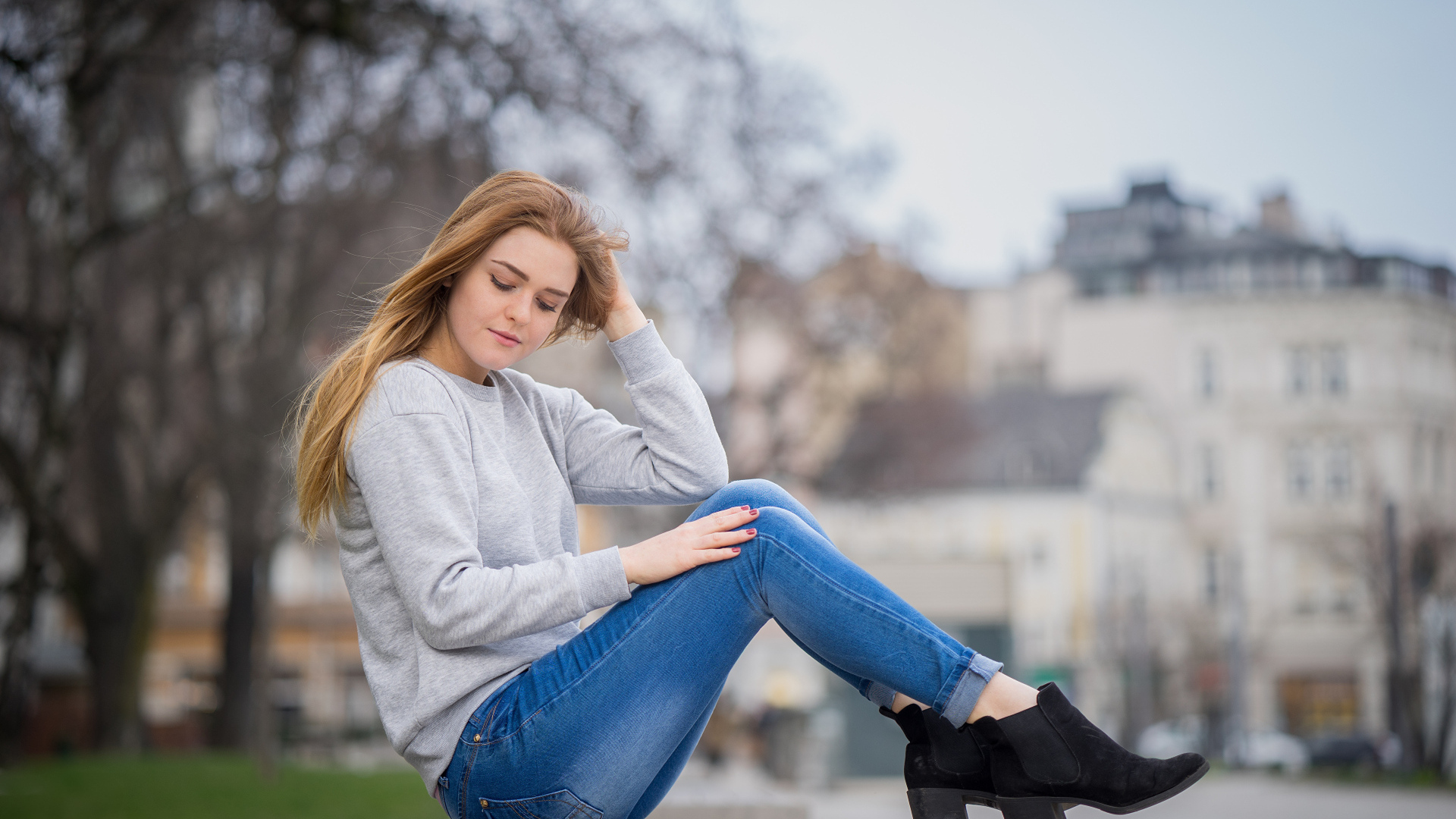 Милая девушка в синих джинсах сидит на лавке