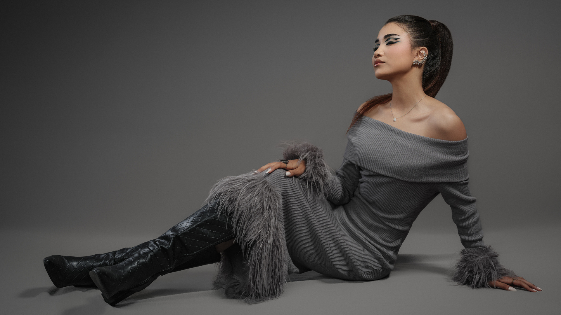 Девушка в платье и длинных черных сапогах на сером фоне