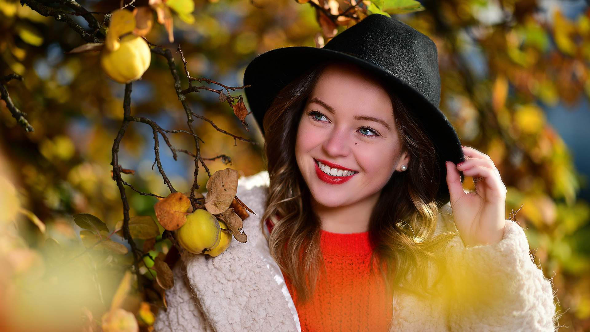 Улыбающаяся девушка в черной шляпе у дерева с яблоками