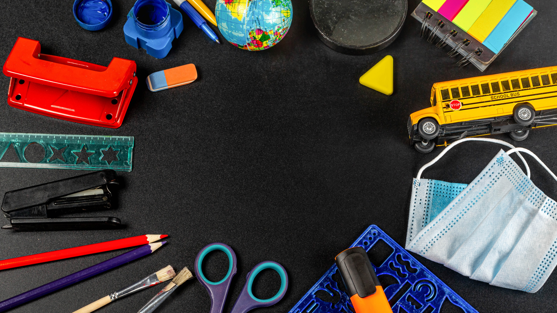 Канцелярские предметы, глобус и игрушечный автобус на черном фоне