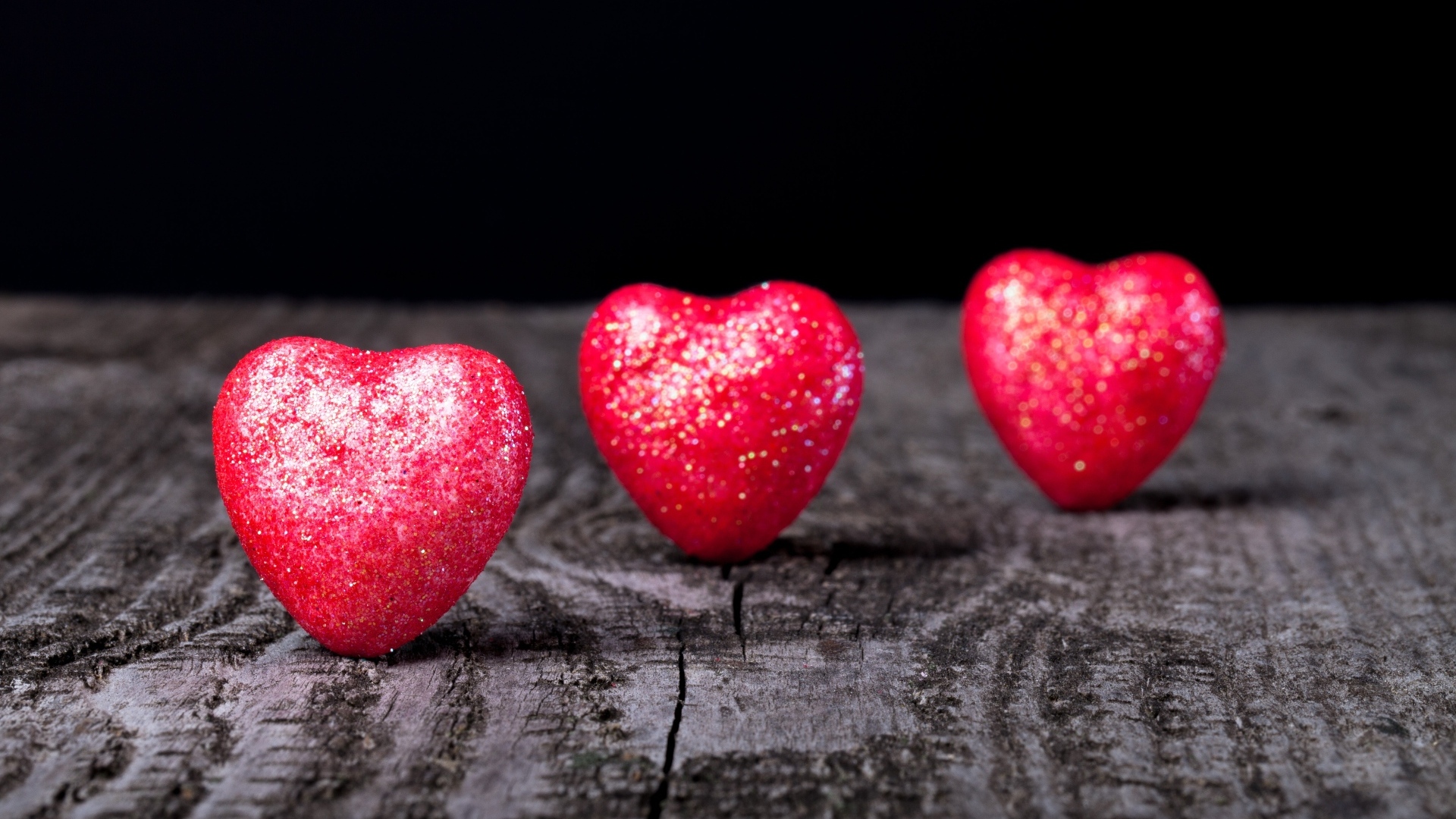 Три блестящих красных сердца на деревянном столе