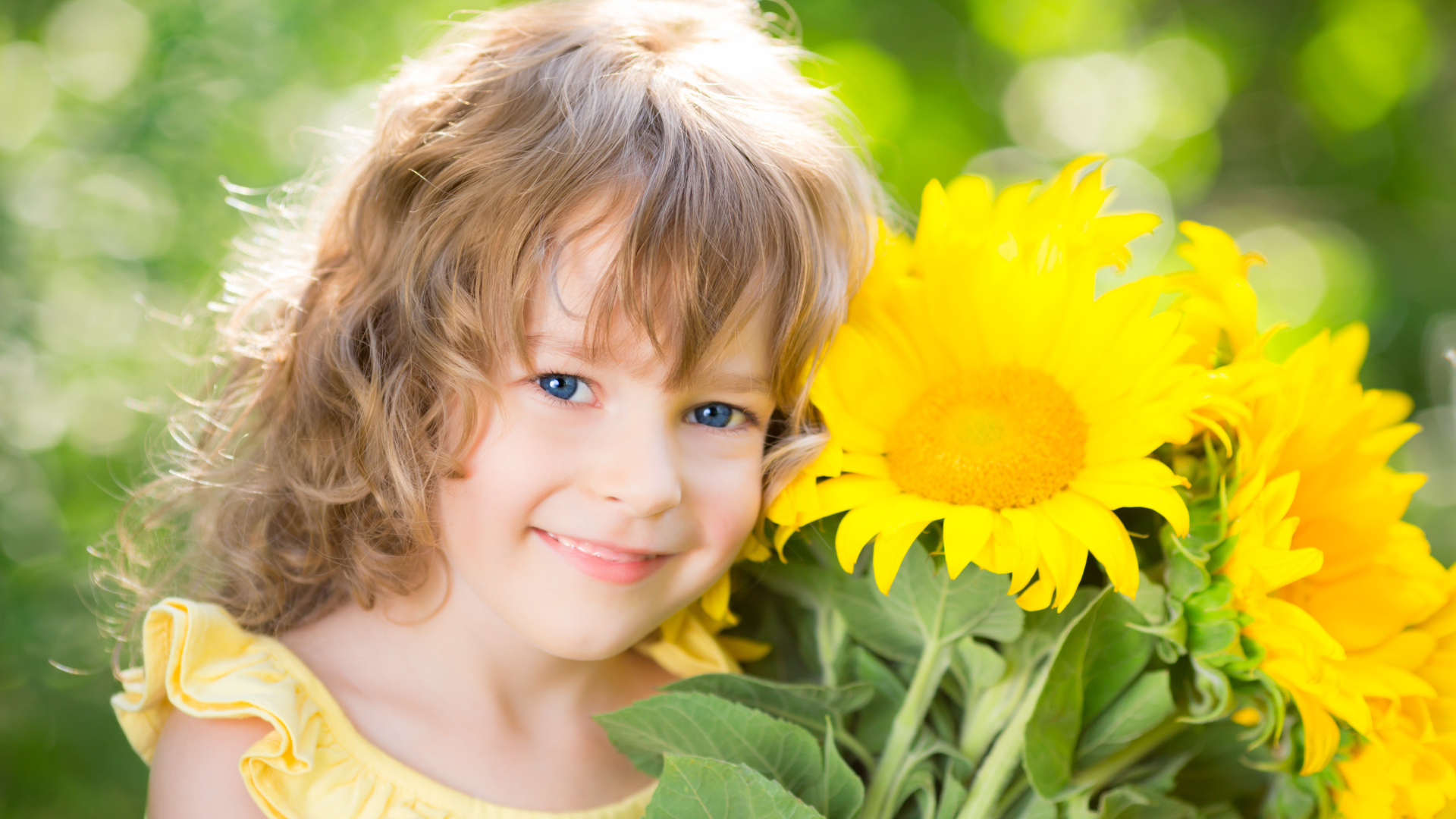 Красивая голубоглазая девочка с букетом подсолнухов