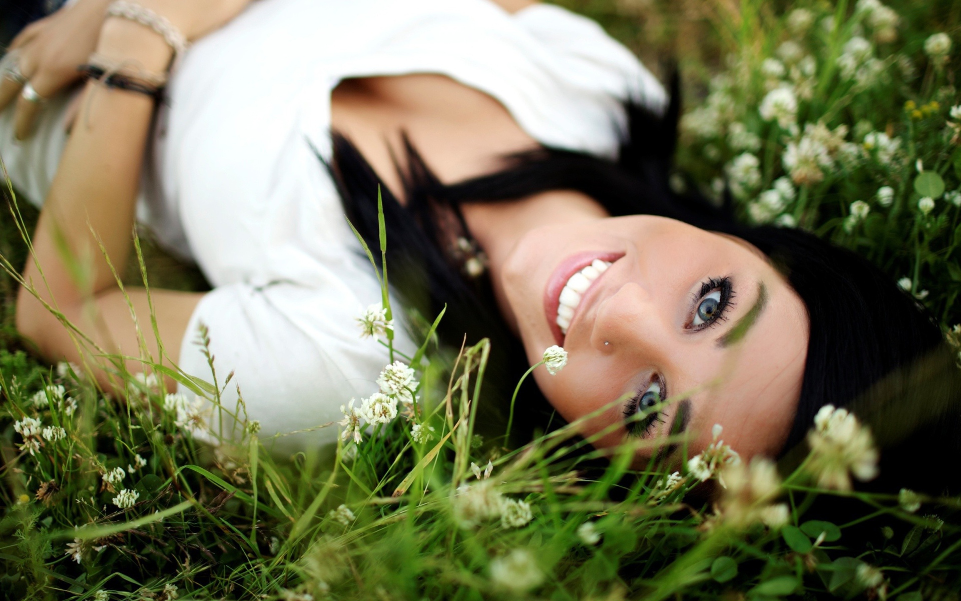 Девушка брюнетка с пирсингом в носу лежит в траве