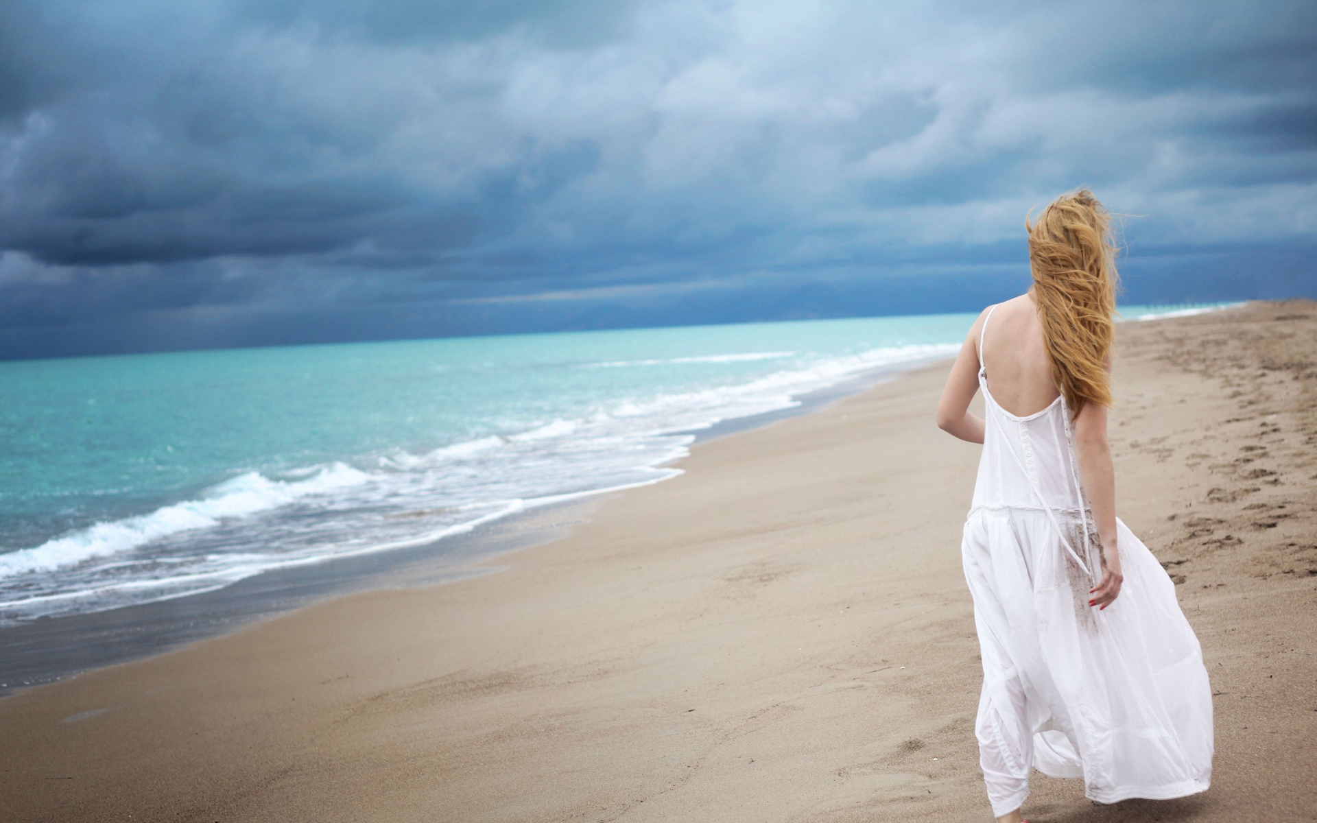 Девушка в белом платье идет по пляжу