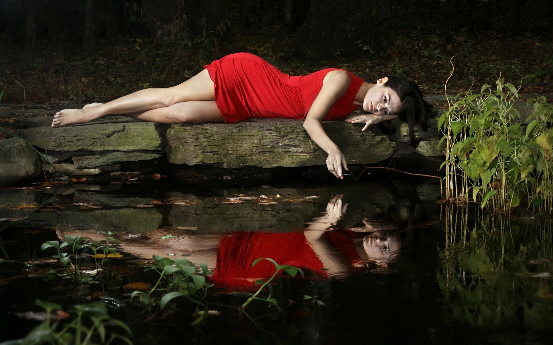 Девушка в красном платье лежит на камне у водоема