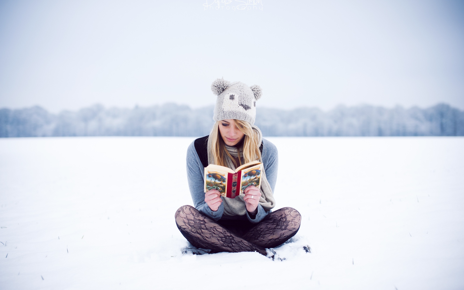 Девушка читает книгу сидя на снегу