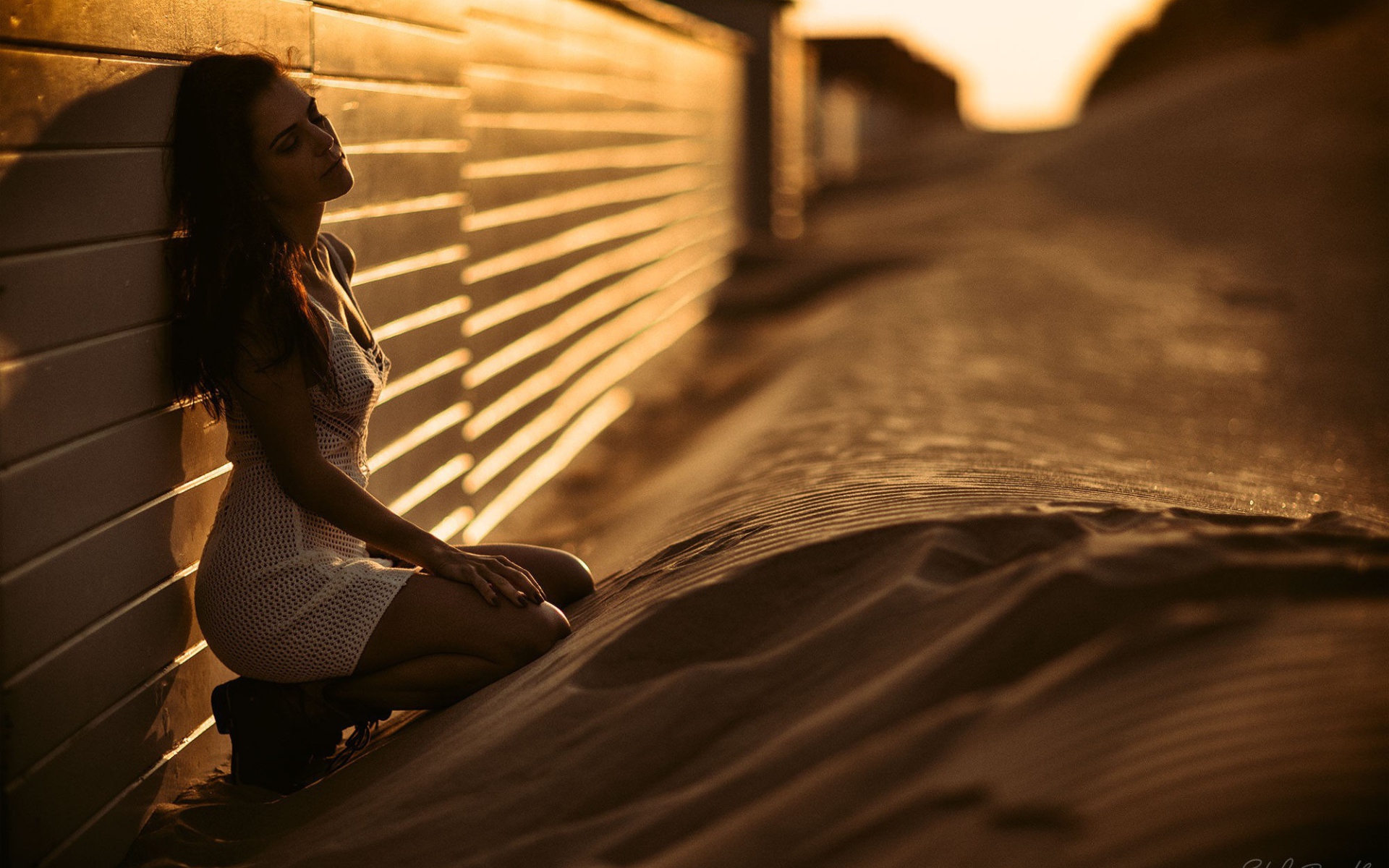 Девушка сидит на песке у забора