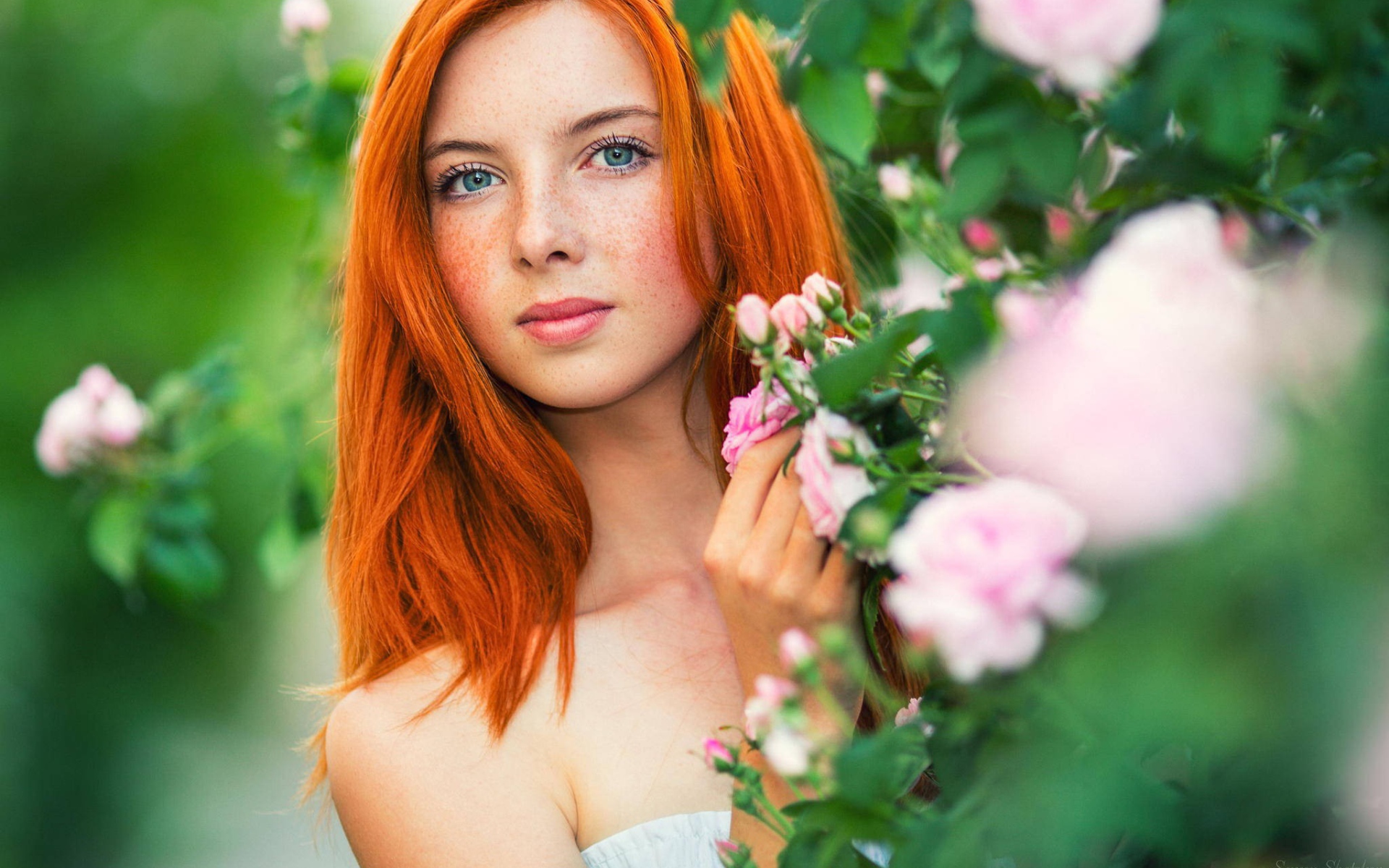 Red-haired girl hides behind the flowering branches